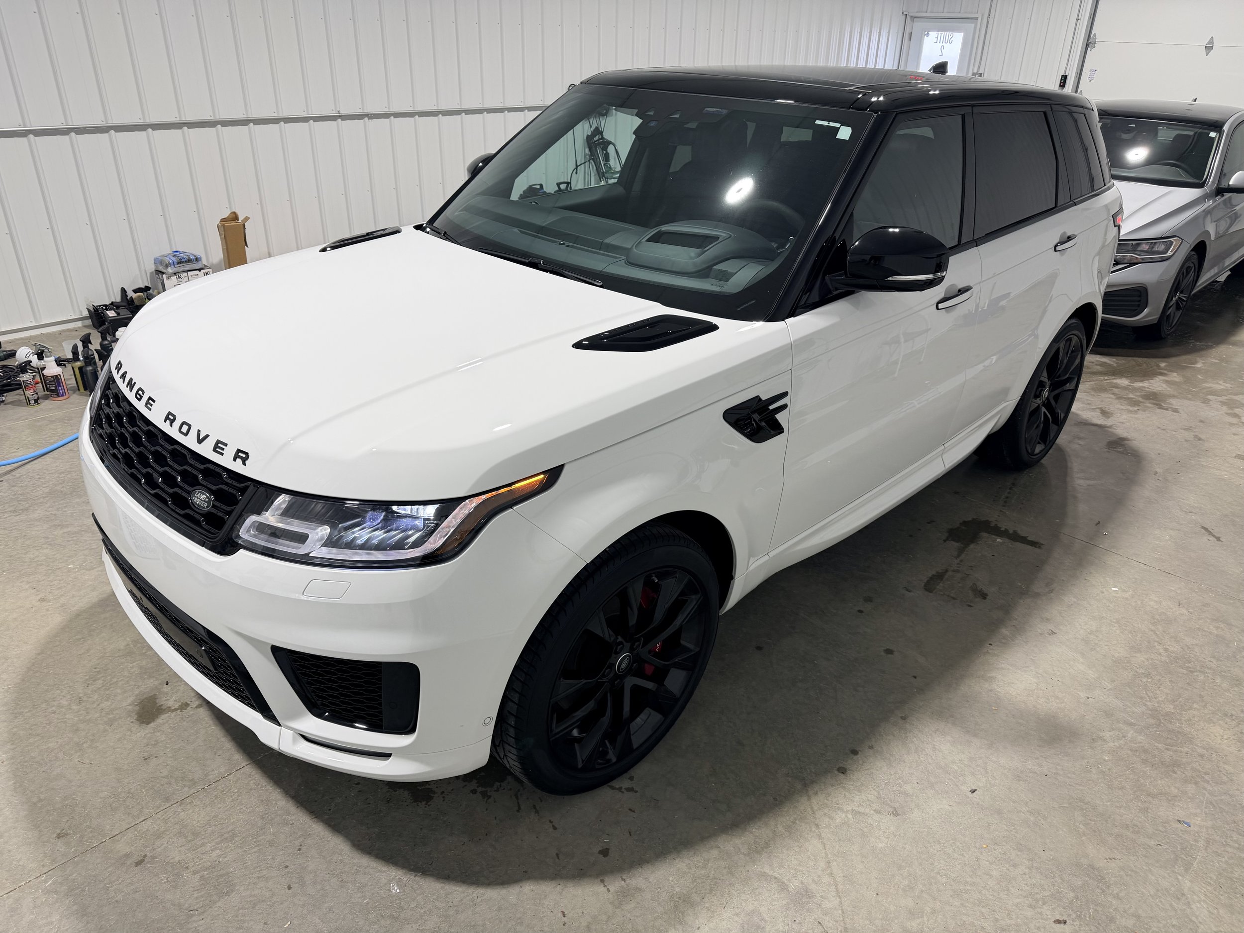 White Range Rover SUV with black wheels and black roof, parked inside a garage with another silver car behind it.