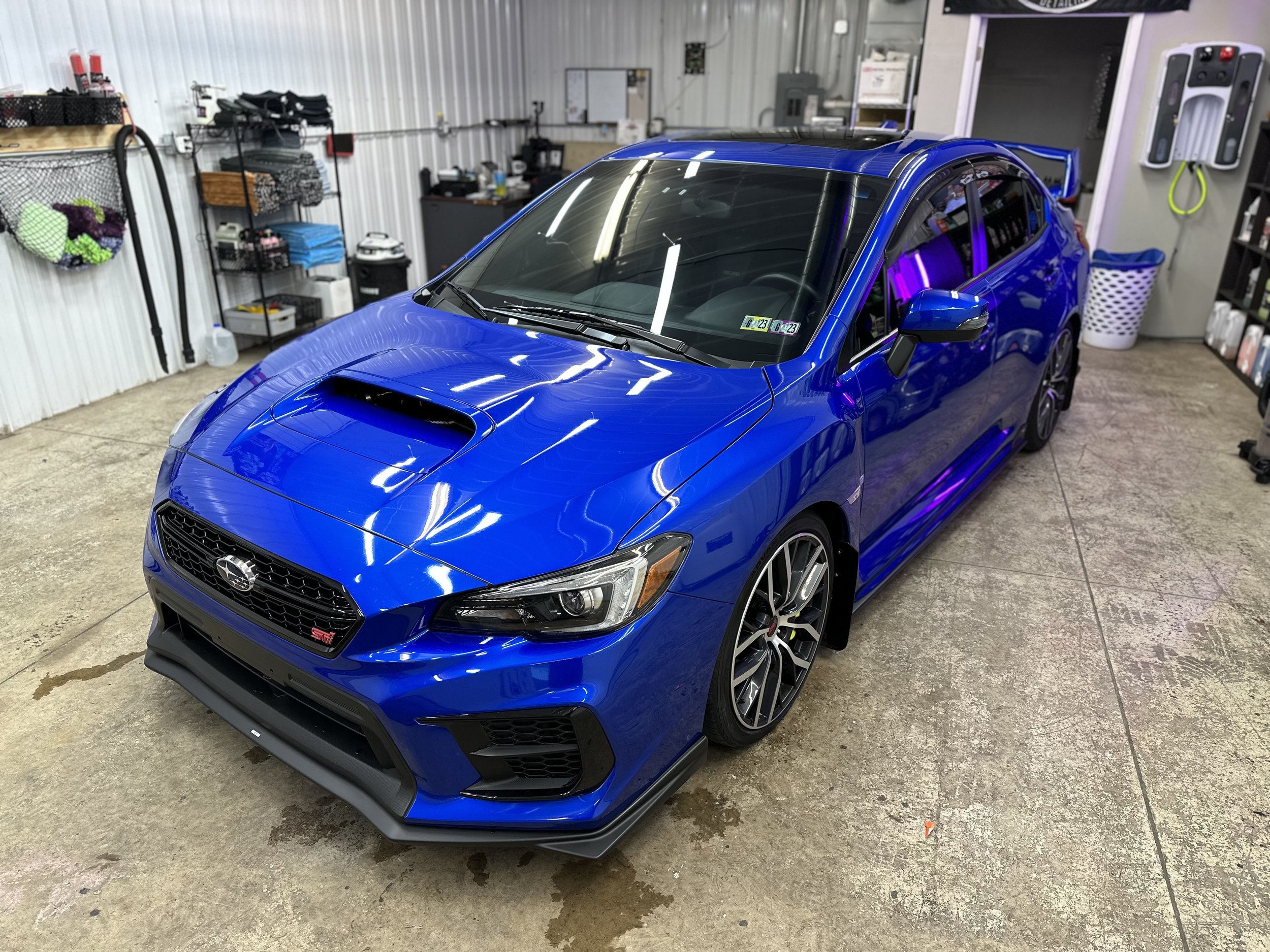 A blue Subaru WRX STI parked inside a garage with work tools and supplies on the walls.