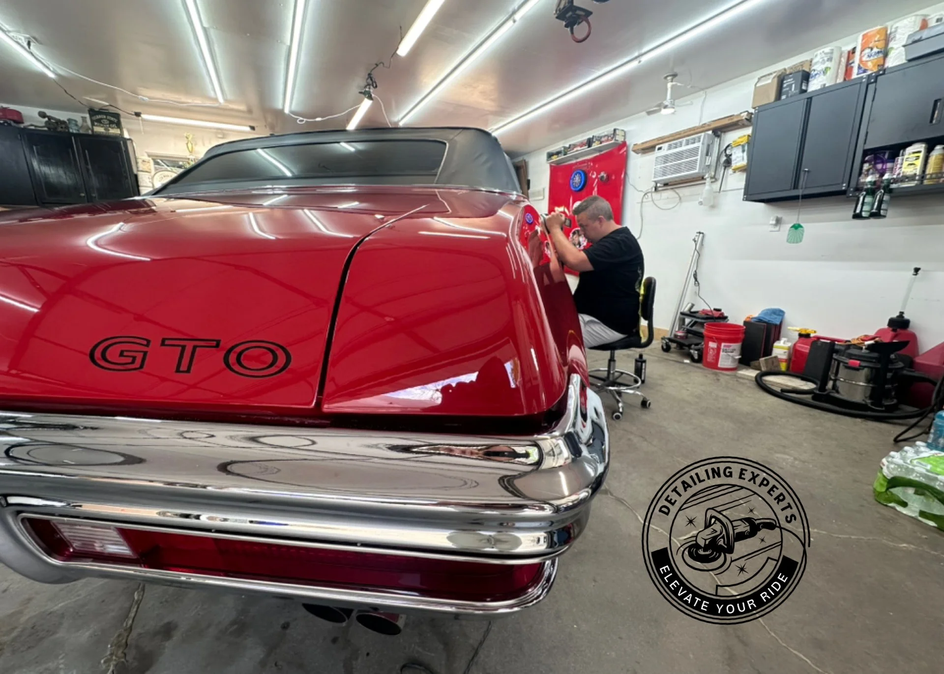 Man working on a red GTO car in a garage, with various tools and equipment around.