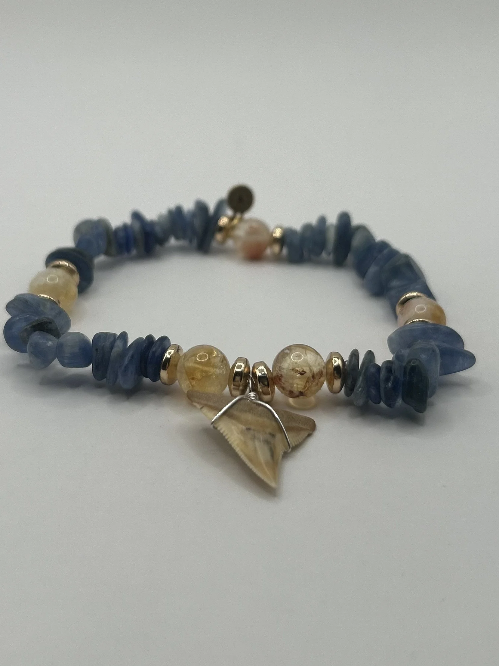 Beaded necklace with blue, beige, and gold beads, and a shell pendant on a white background.