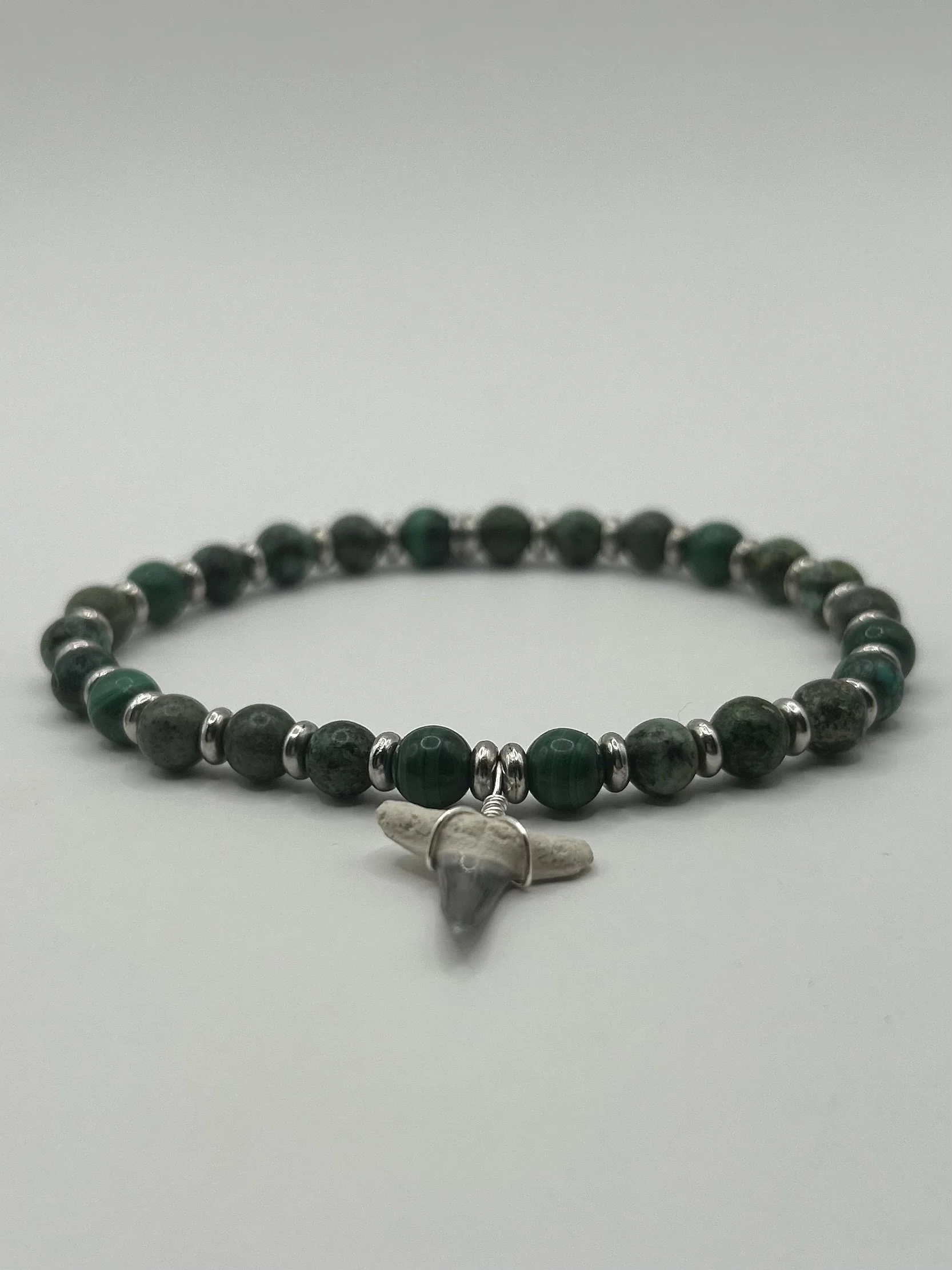 Beaded bracelet with green and black beads and a small animal skull pendant.