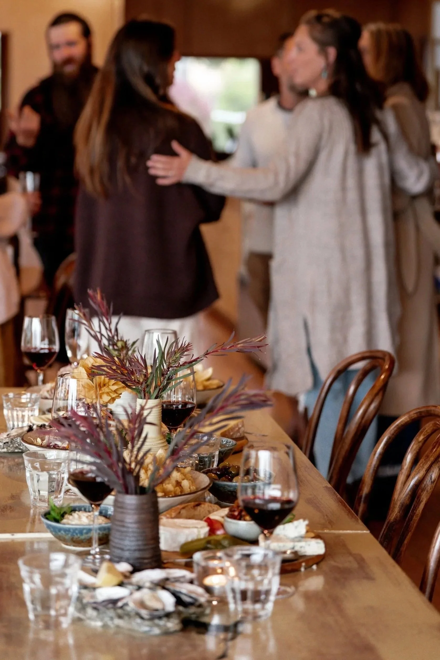 A dining table set with wine glasses, plates of food, and floral centerpieces, with people in the background socializing.