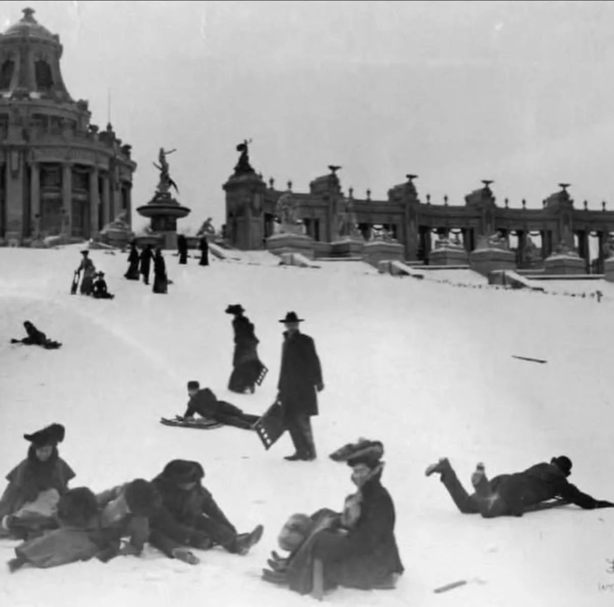 Image of people sledding in Victorian clothing circa 1905 in St. Louis, using folding chairs as sleds in front of Art Hill in Forest Park. Black and White.