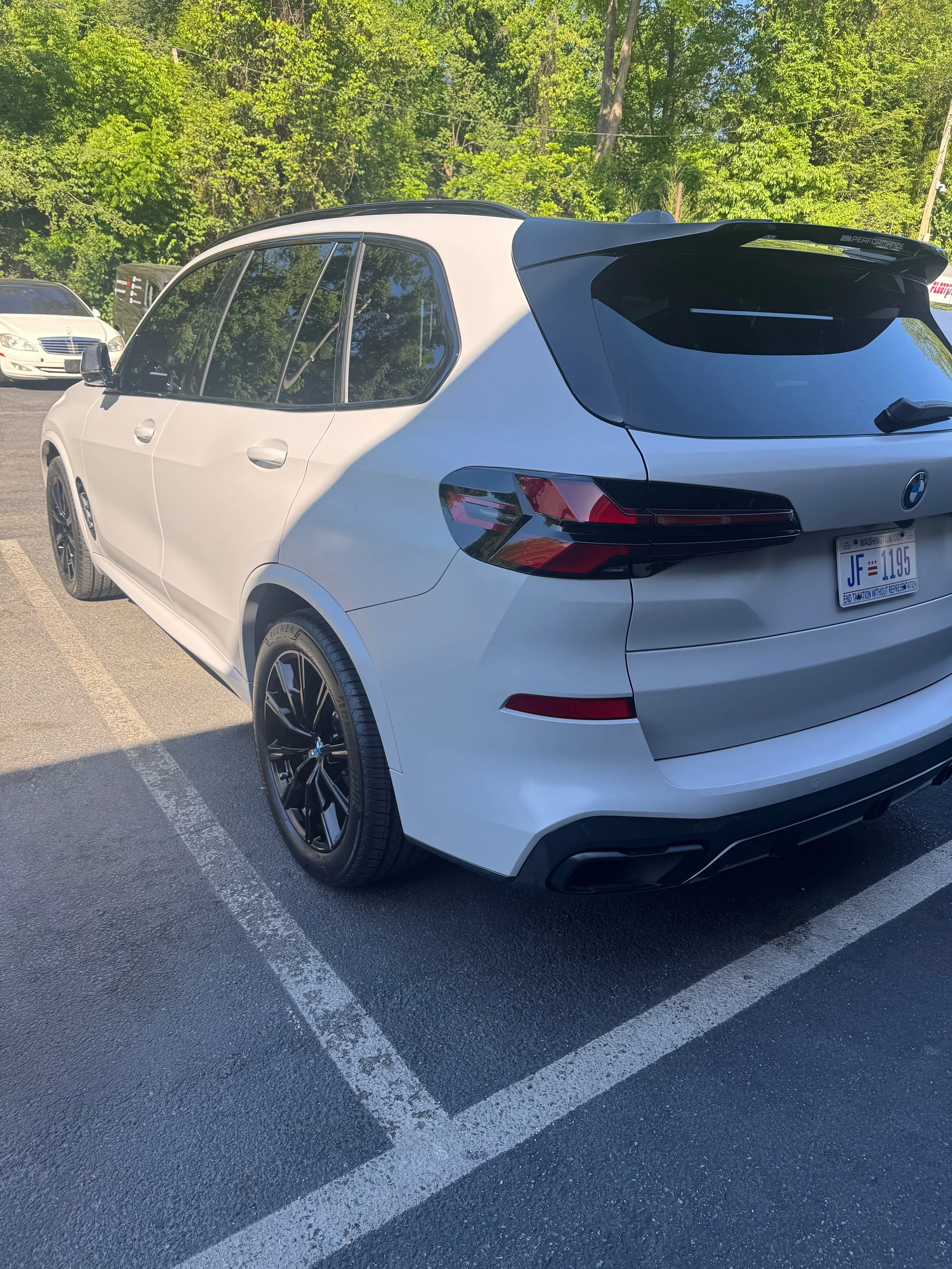 White BMW SUV parked in a parking lot with trees in the background car wrap