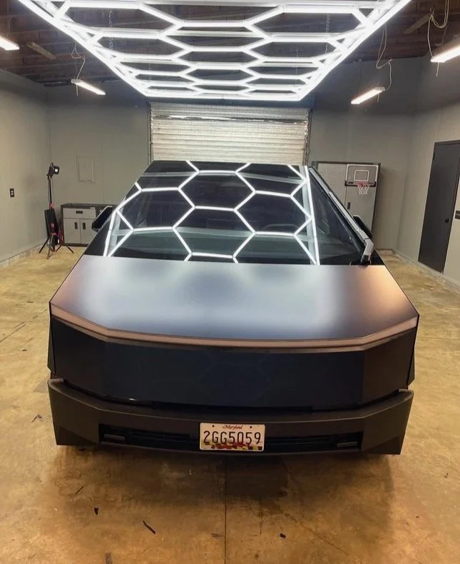 A futuristic black car with a hexagon-patterned glass roof and glowing hexagon LED ceiling lights in a garage.