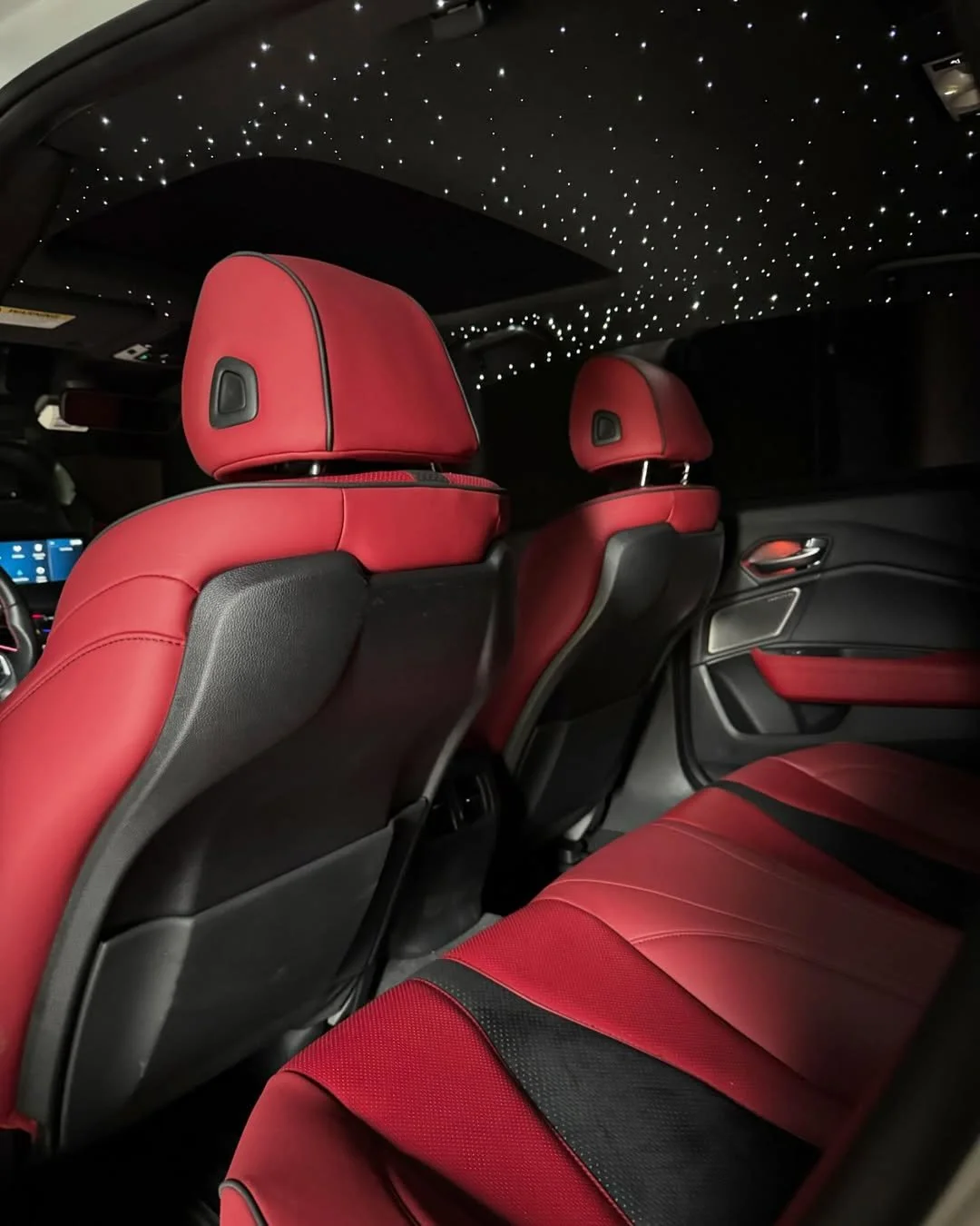 The interior of a luxury car with red and black leather seats and a starry sky ceiling lighting effect.