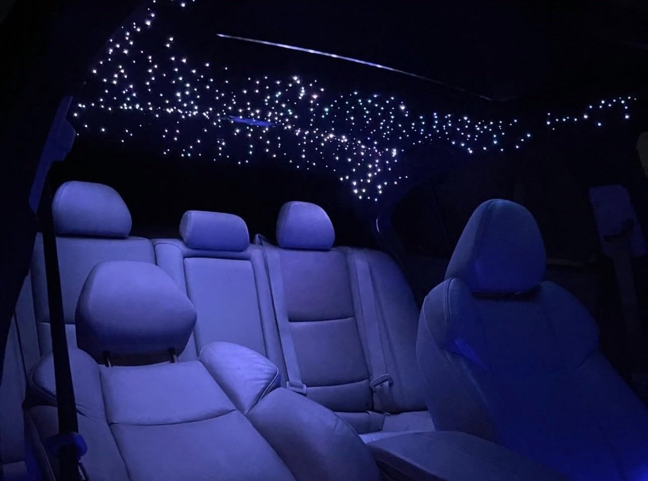 Interior of a car showing illuminated star-like ceiling lights and leather seats.