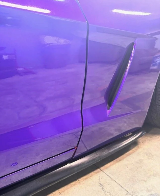 Close-up of a purple car door with a black noose hanging from the door handle.