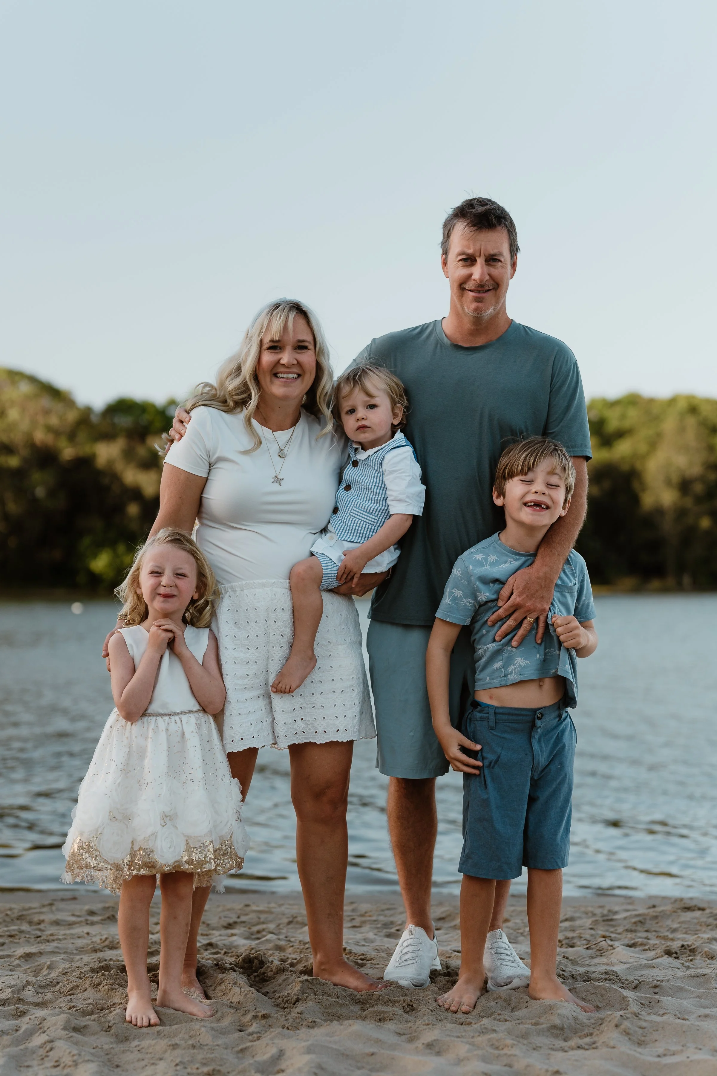 Family of six standing on a sandy beach near a body of water, smiling for a photo.