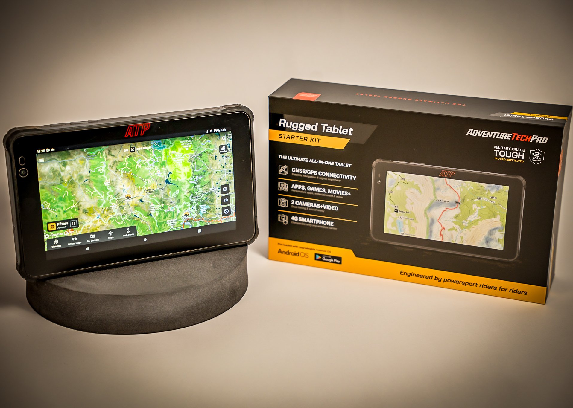 Product photography of the Adventure Tech Pro rugged tablet displayed next to its retail packaging with the screen powered on showing navigation maps.