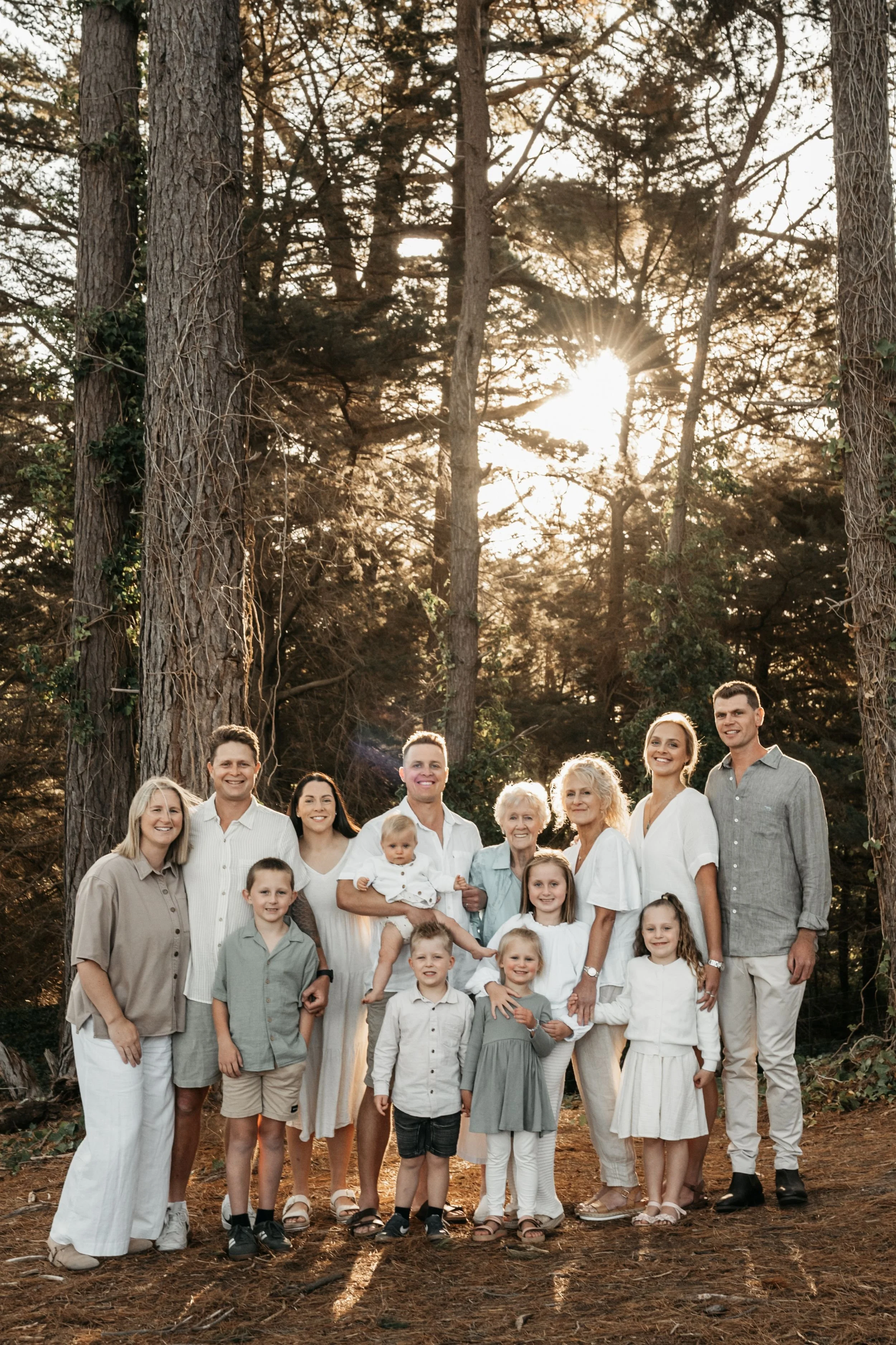 An extended family gather together in the forest with golden back light