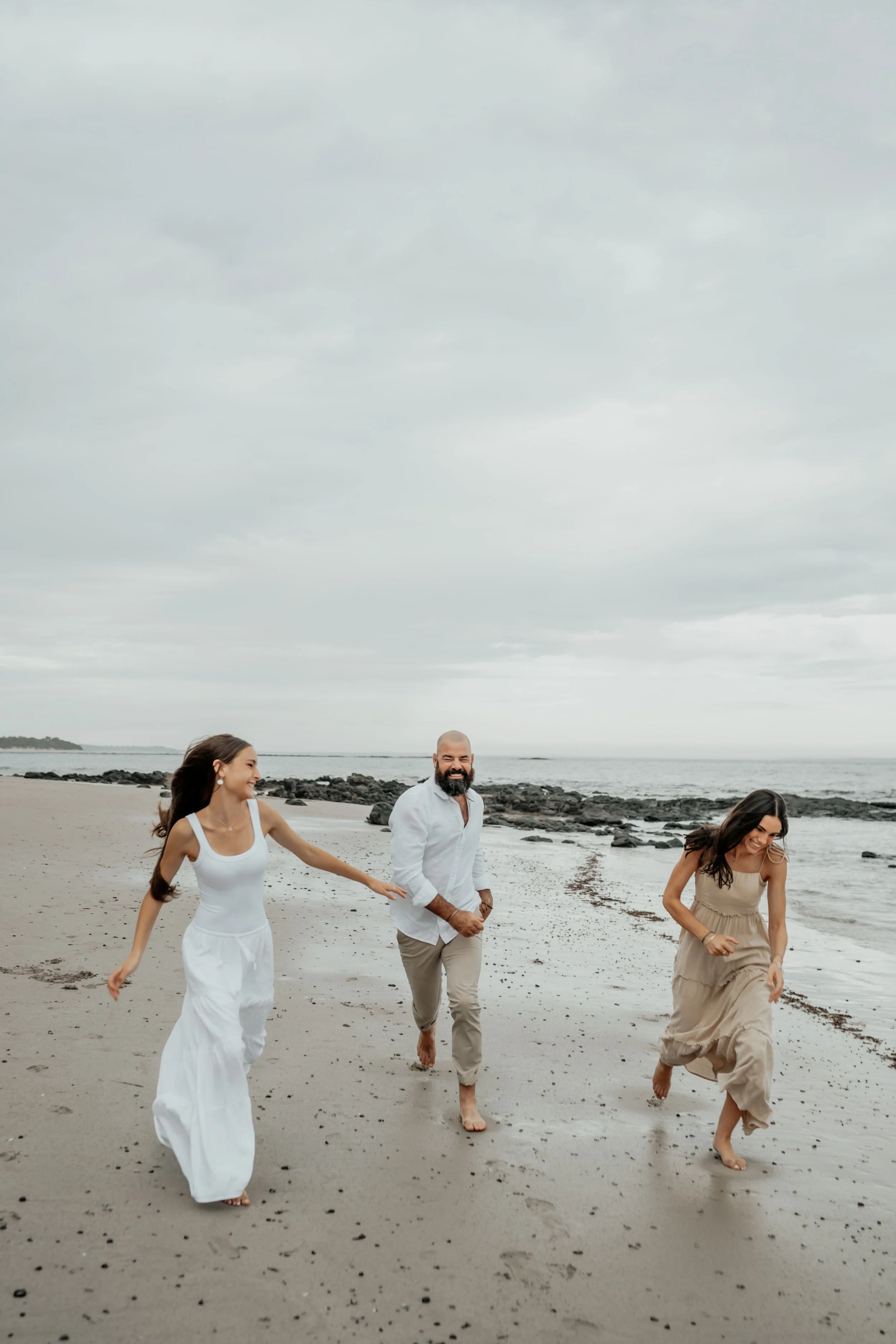 A father running and playing along the beach with his teenage daughters