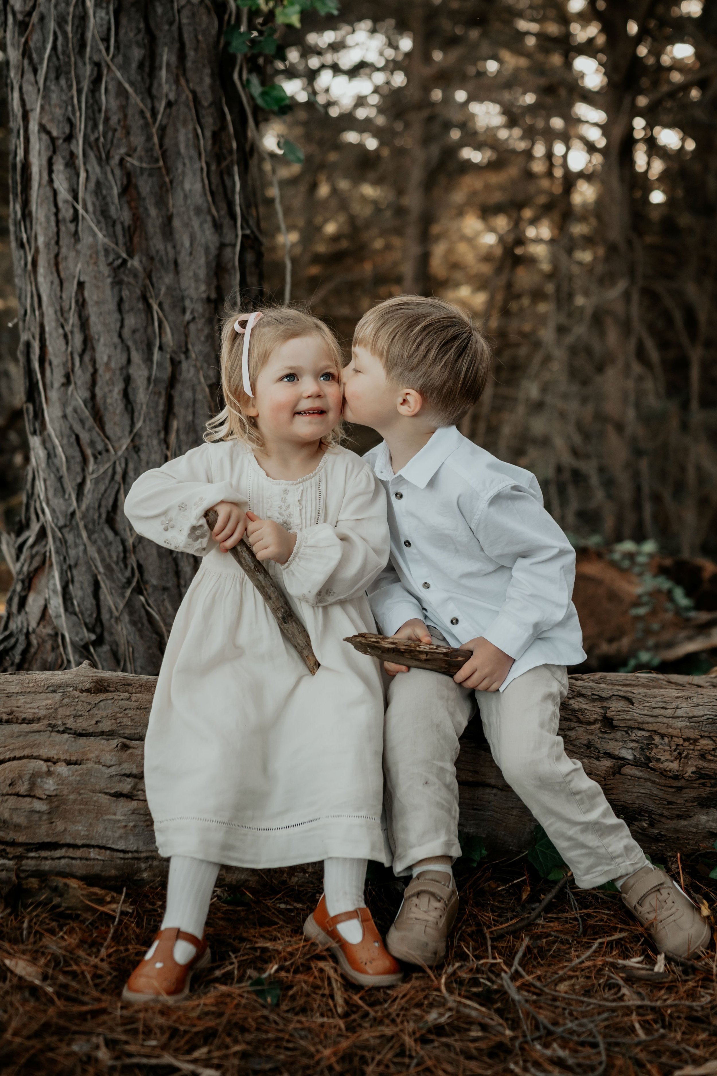Siblings snuggling on a log in the forest. Big brother kissing his little sister