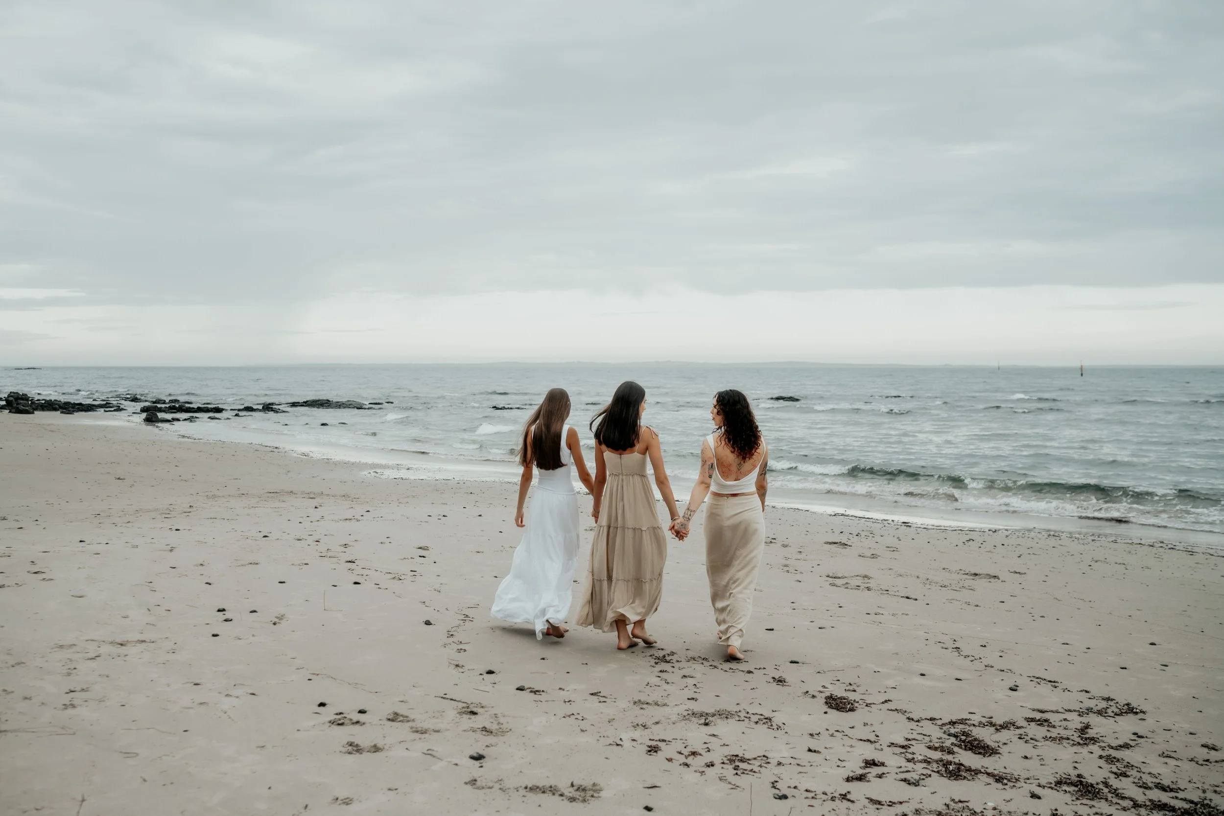 Teenage sisters holding hands and walking towards the water on the beach