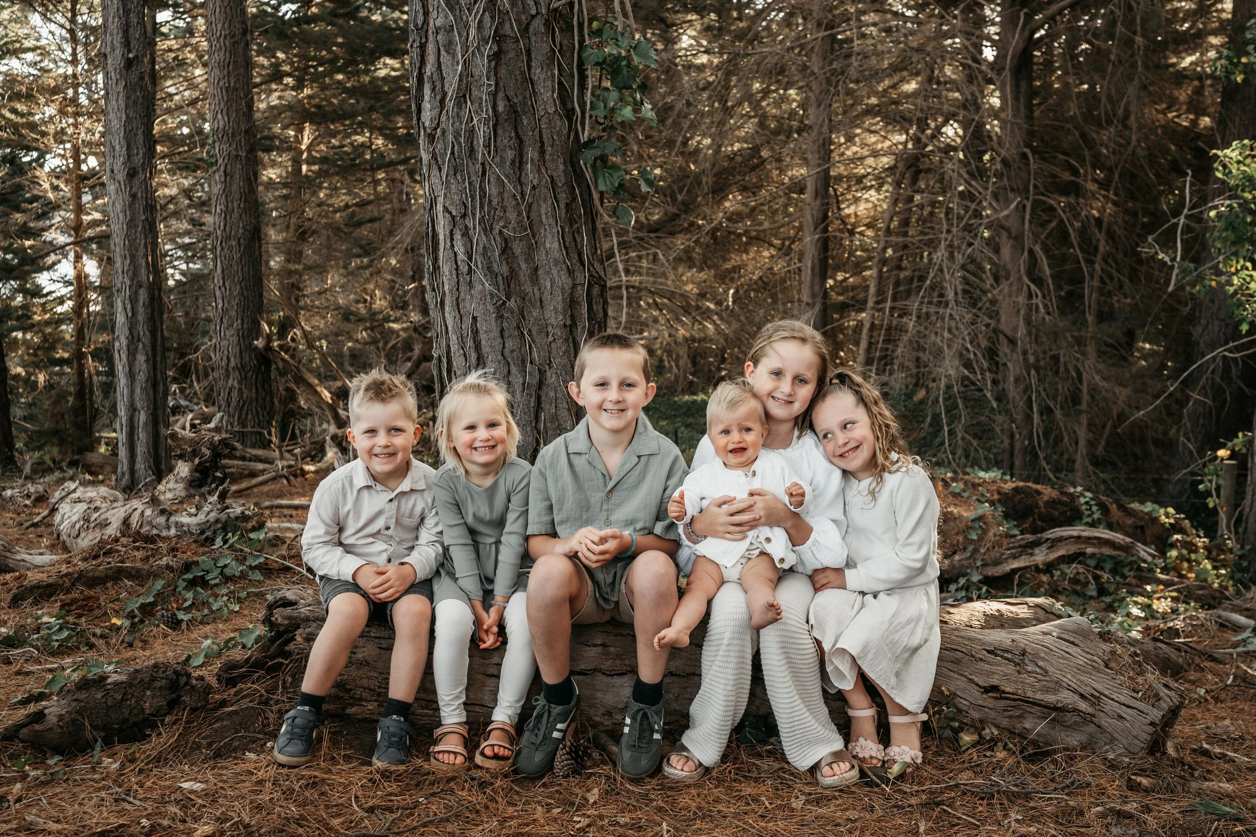 Cousins sit on a log snuggled up and smiling