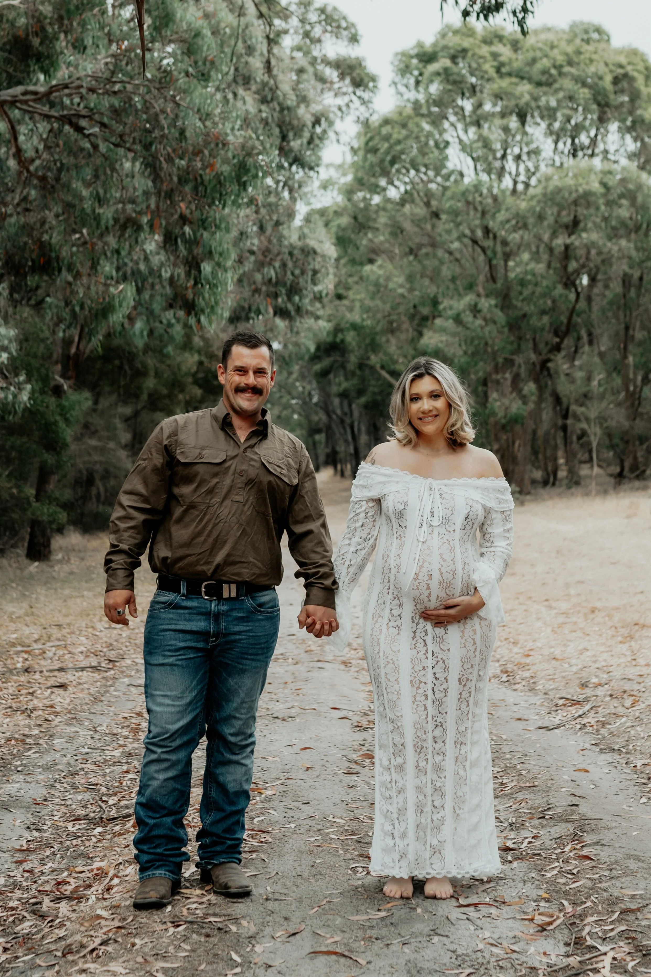 A maternity session with a couple holding hands amongst a bush setting