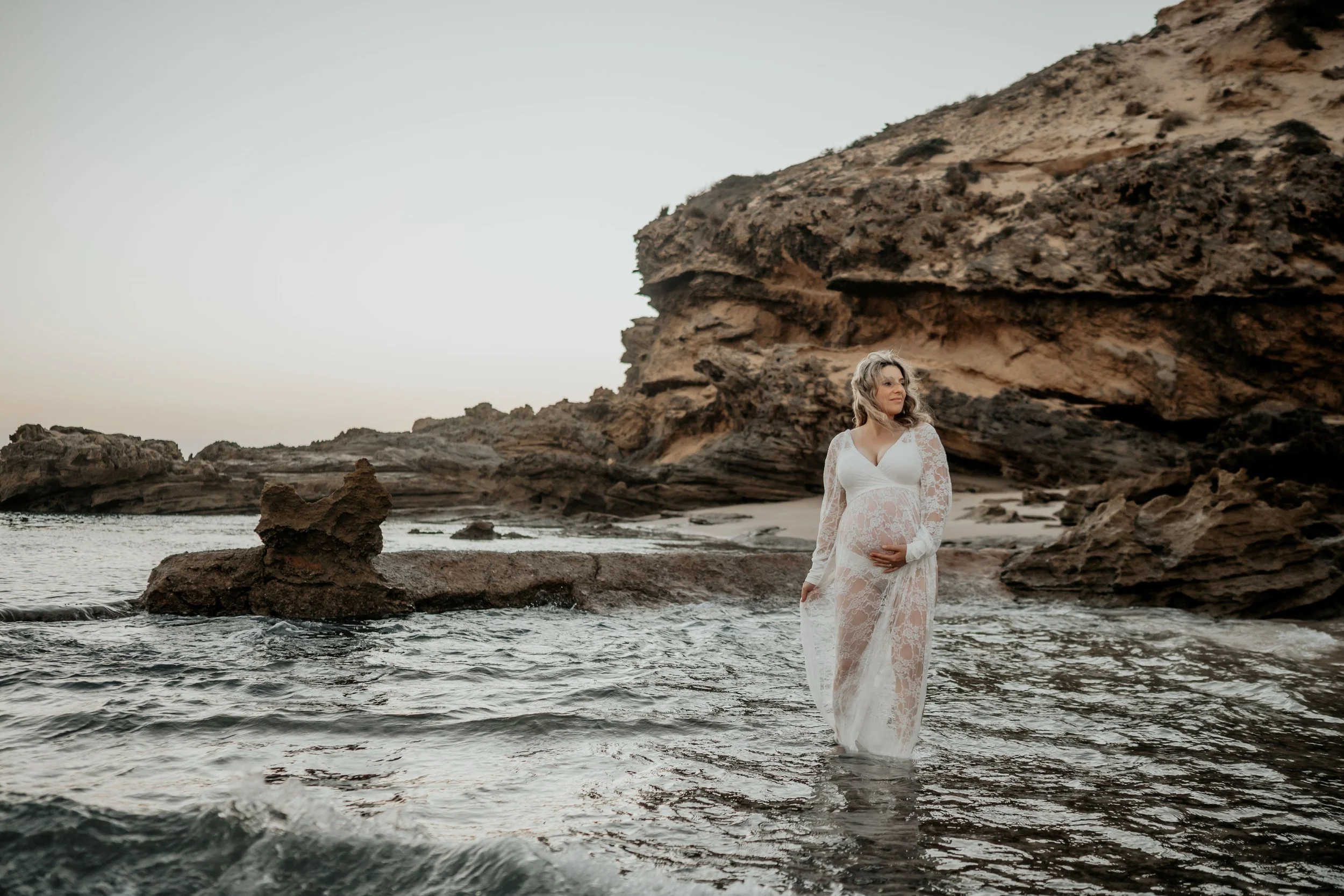 A maternity session with a woman holding her belly and walking through the water