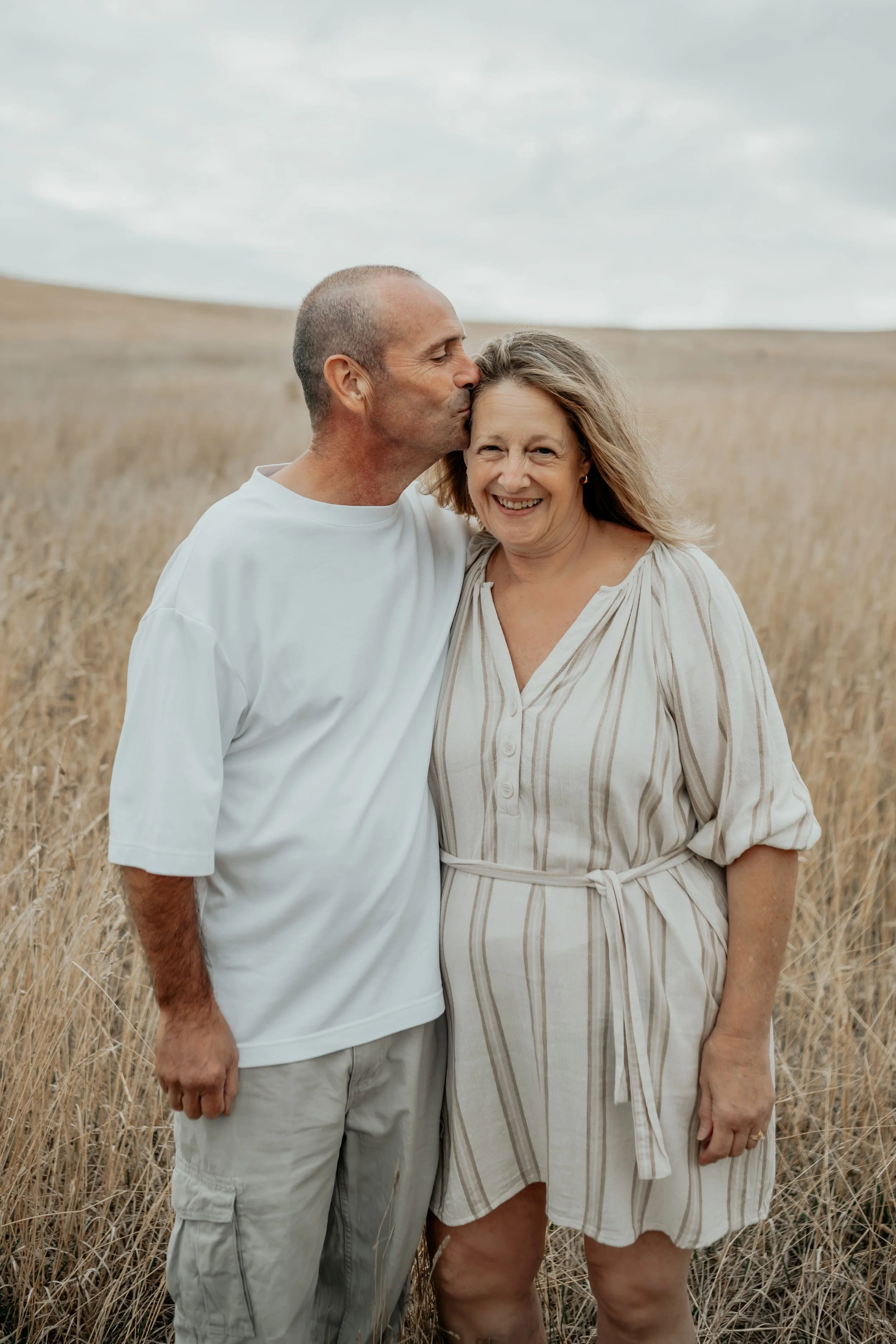 Grandparents, grandfather kissing his wife on the temple in a golden field