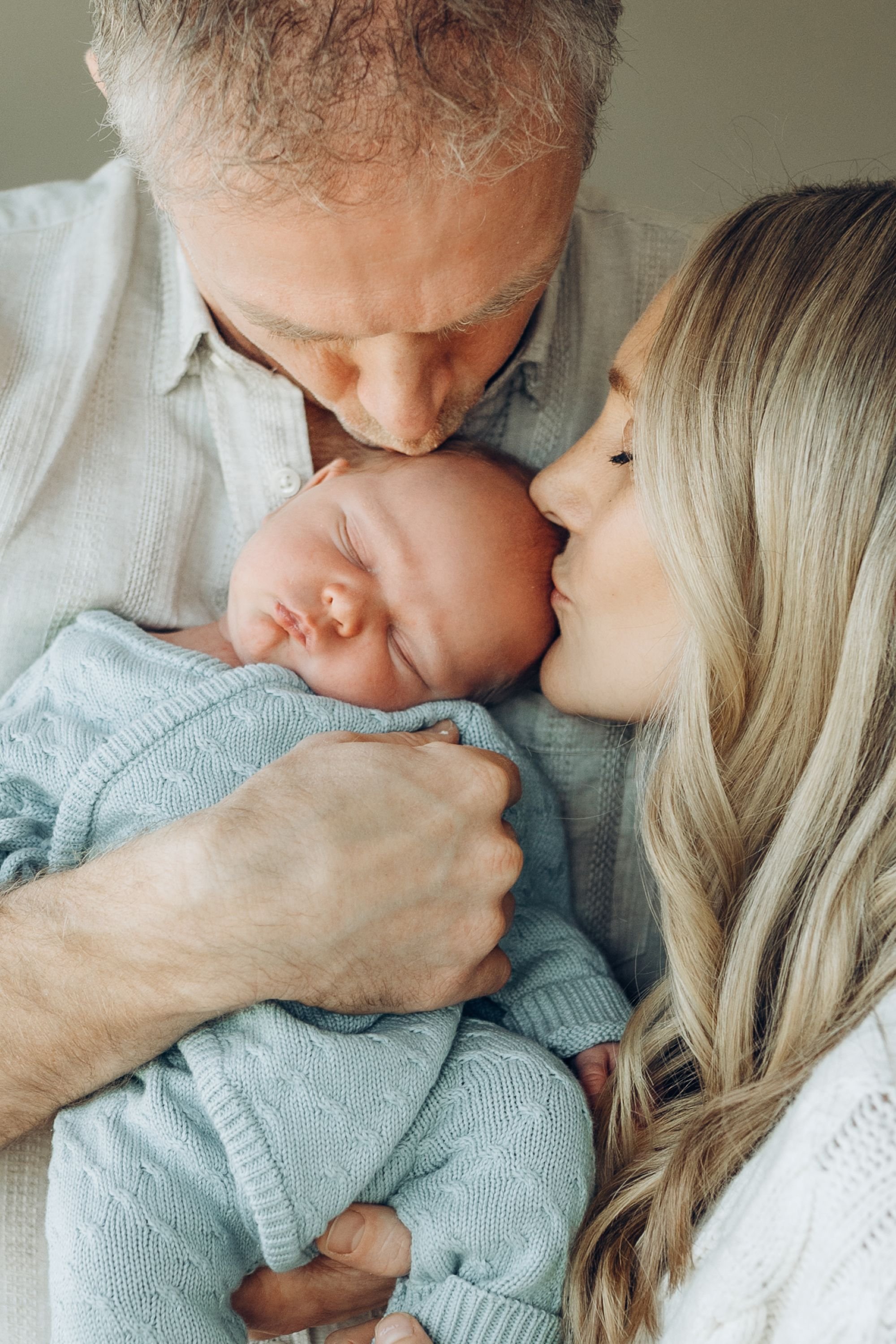 A mum and dad kiss their newborn at the same time during a relaxed newborn photography session in Melbourne