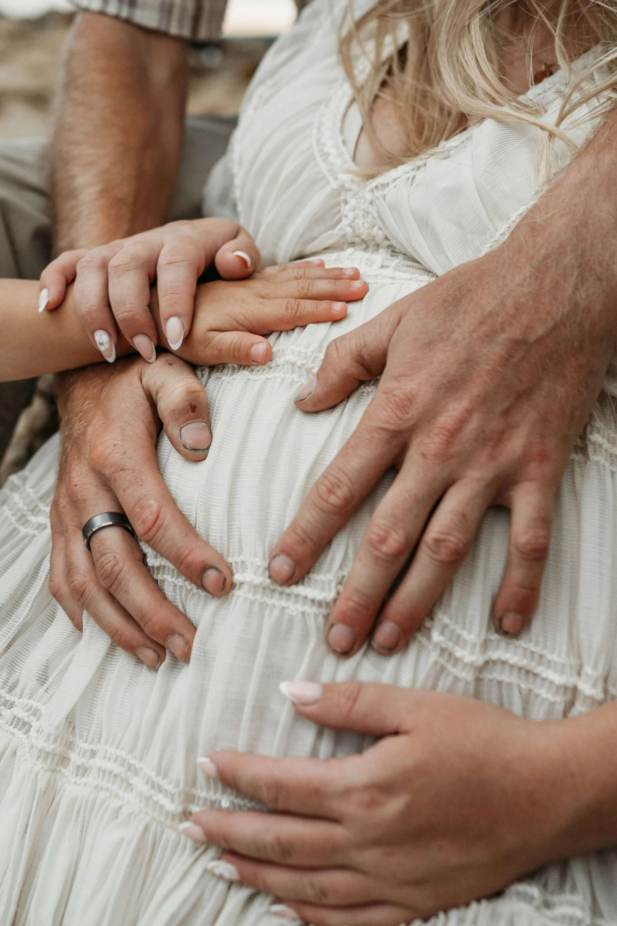 Family hands hold a pregnant belly