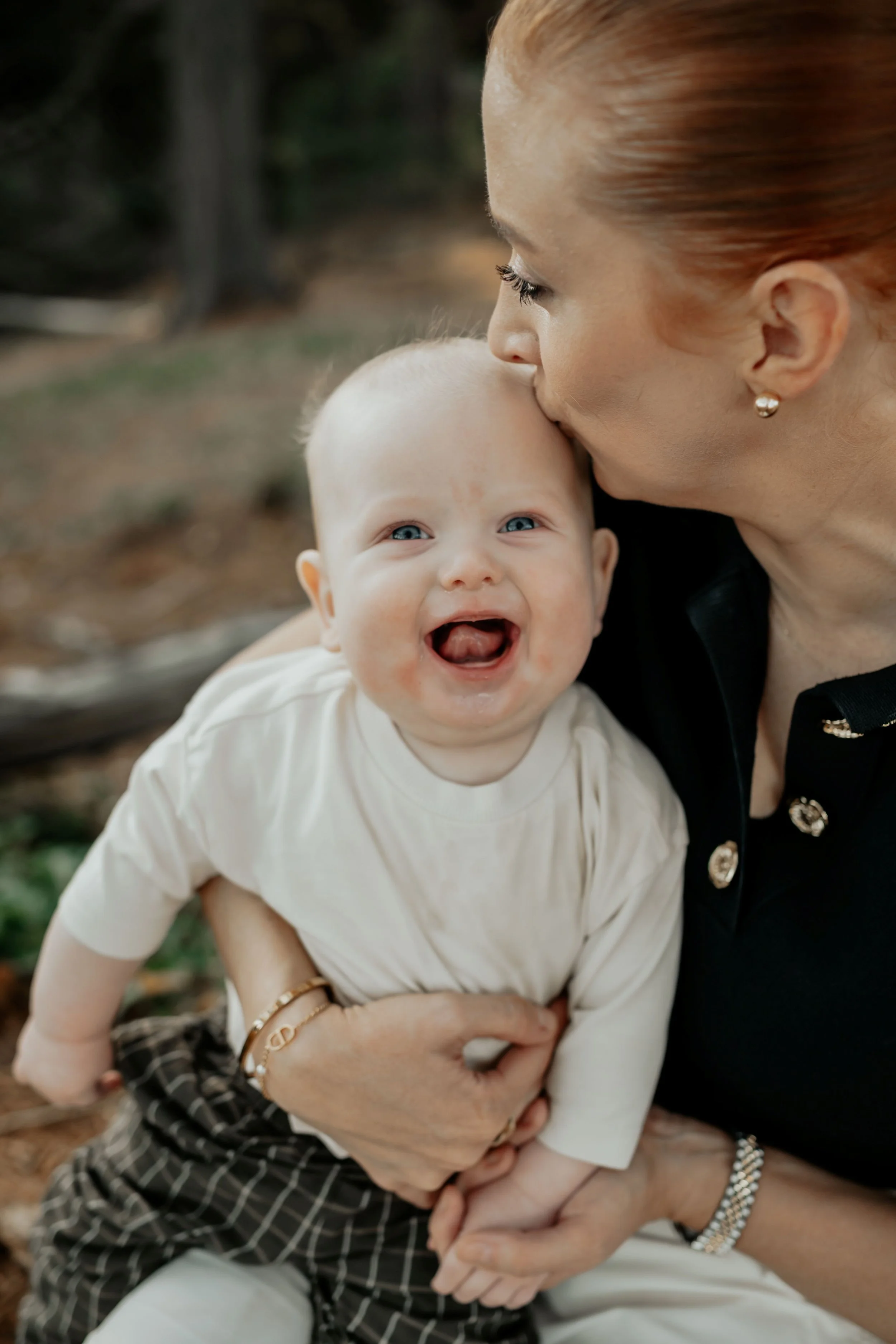 A baby laughs while his mother kisses his head
