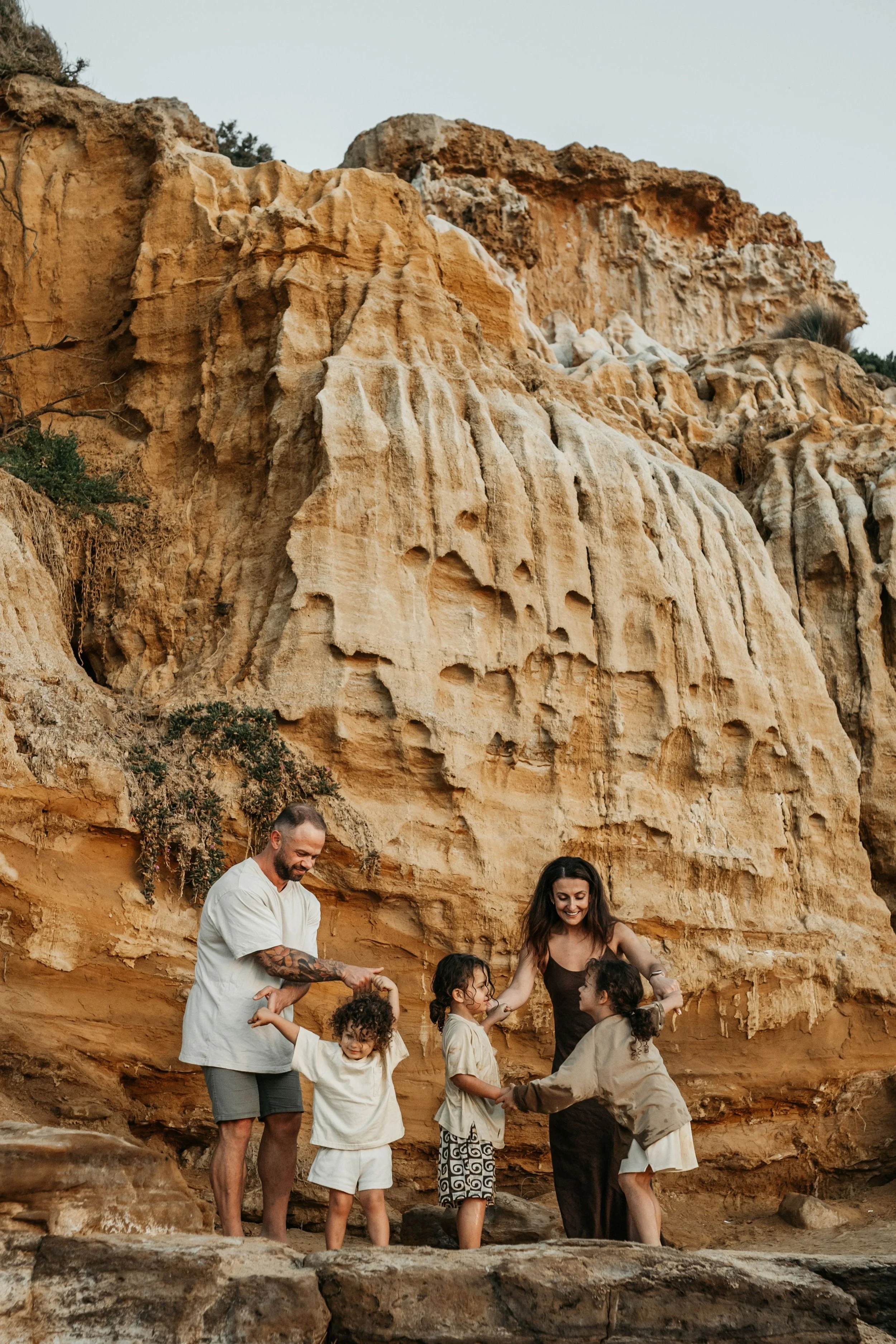 A family dancing together against a cliff wall at Black Rock beach