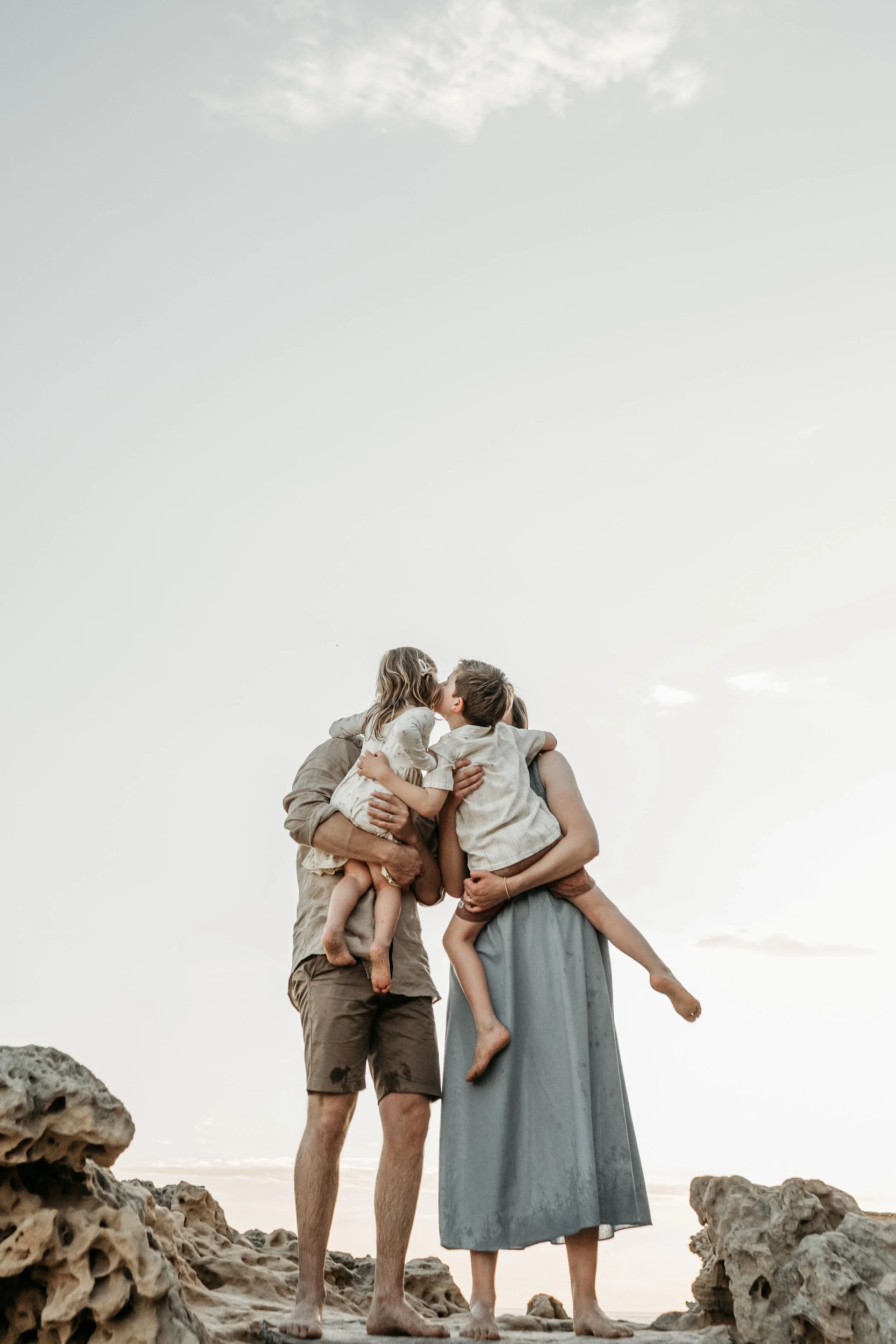 A mother and father holding their two children who are kissing