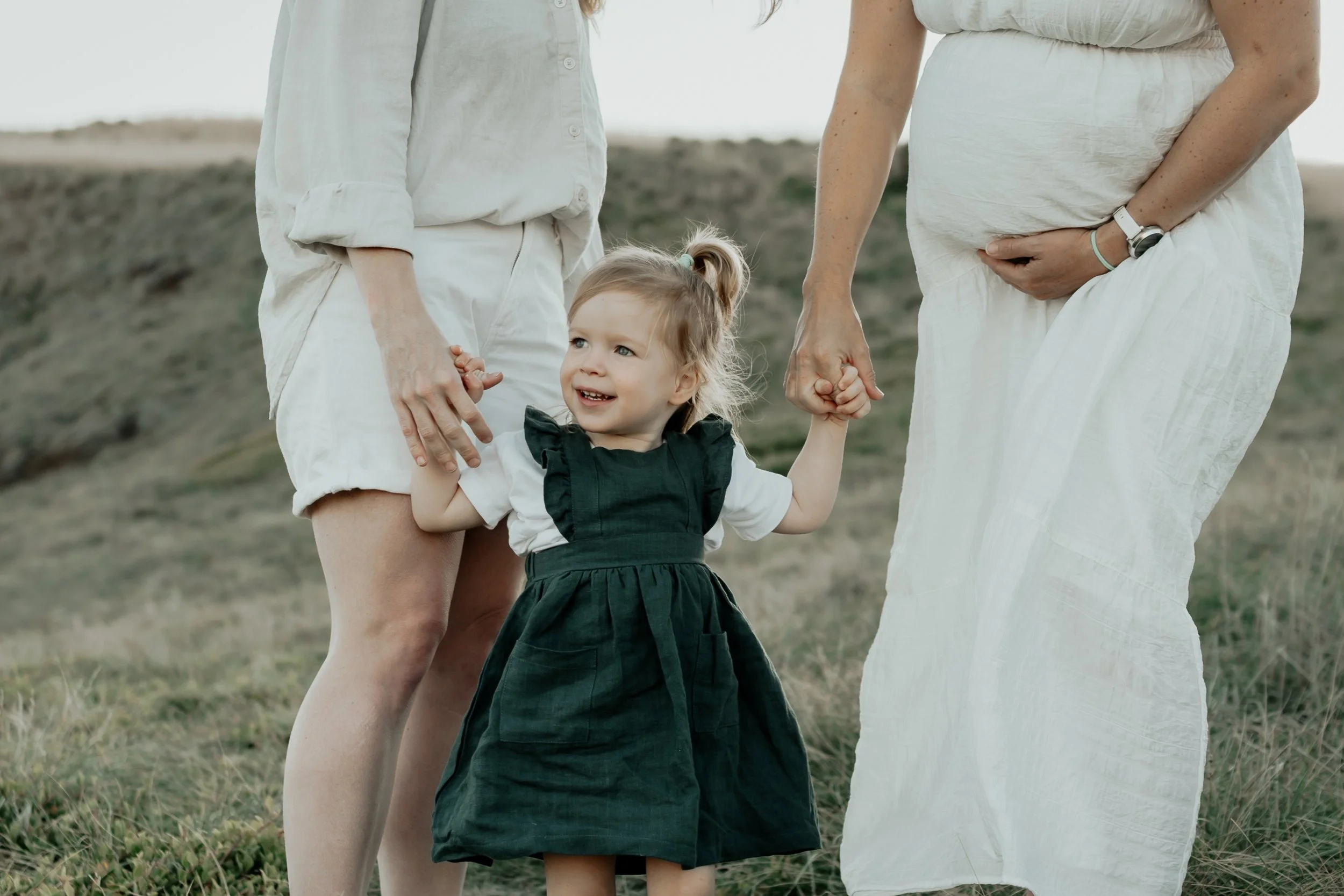 A girl holding both of her mother's hands. One mother pregnant and her belly in view.