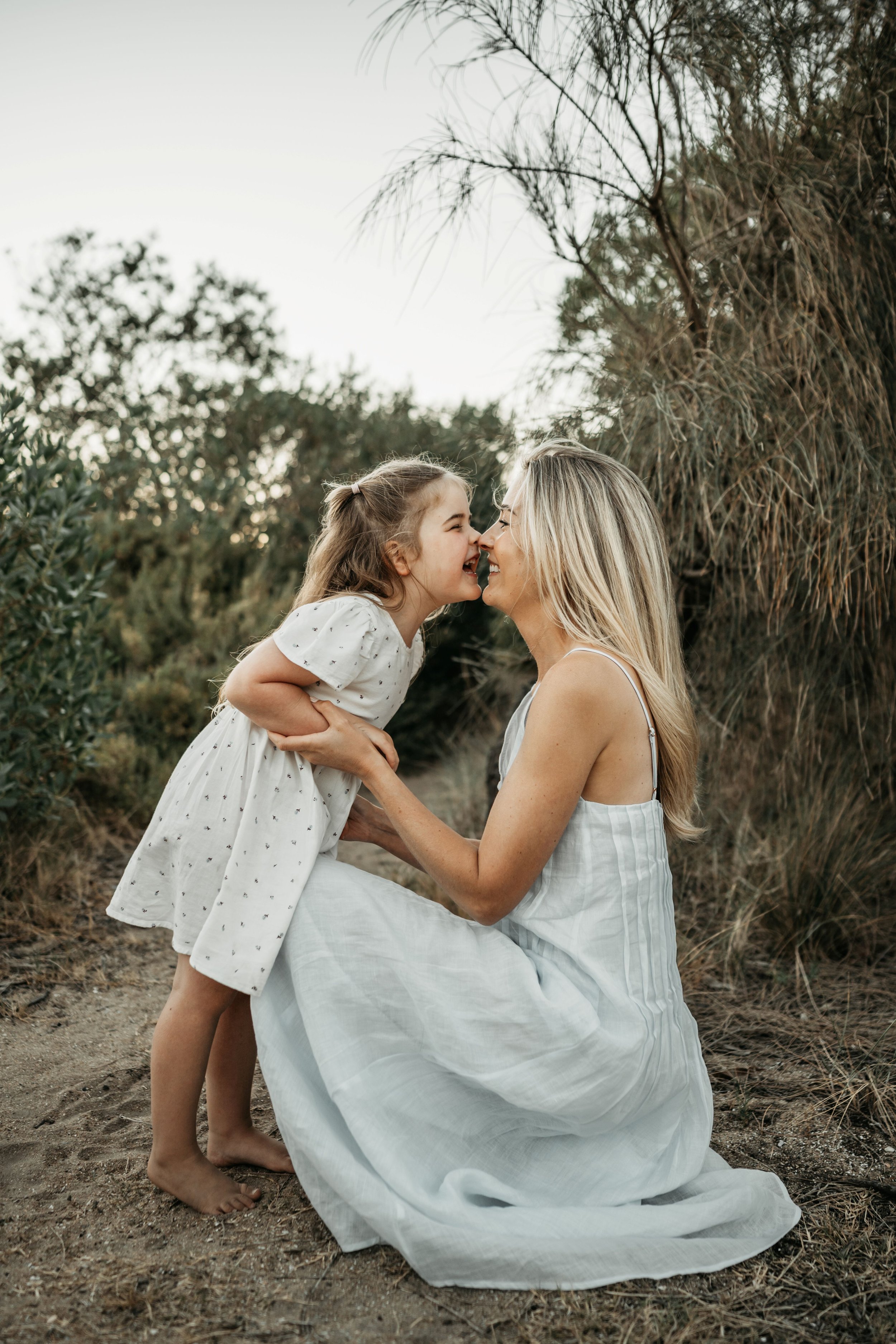 A mother and daughter laughing while doing nosey nuzzles amongst greenery