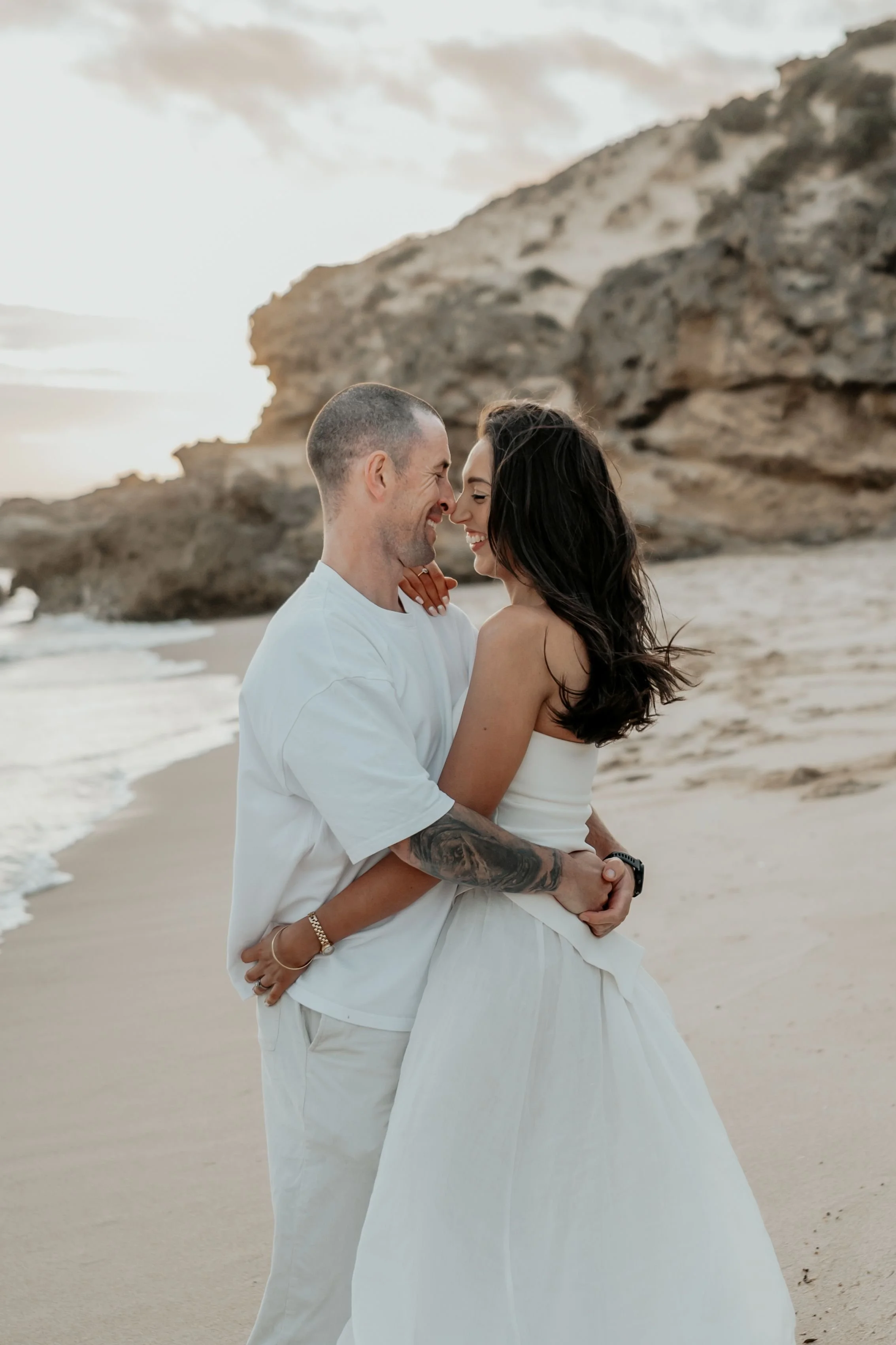 Husband and wife arm in arm touching noses and looking happy on the beach