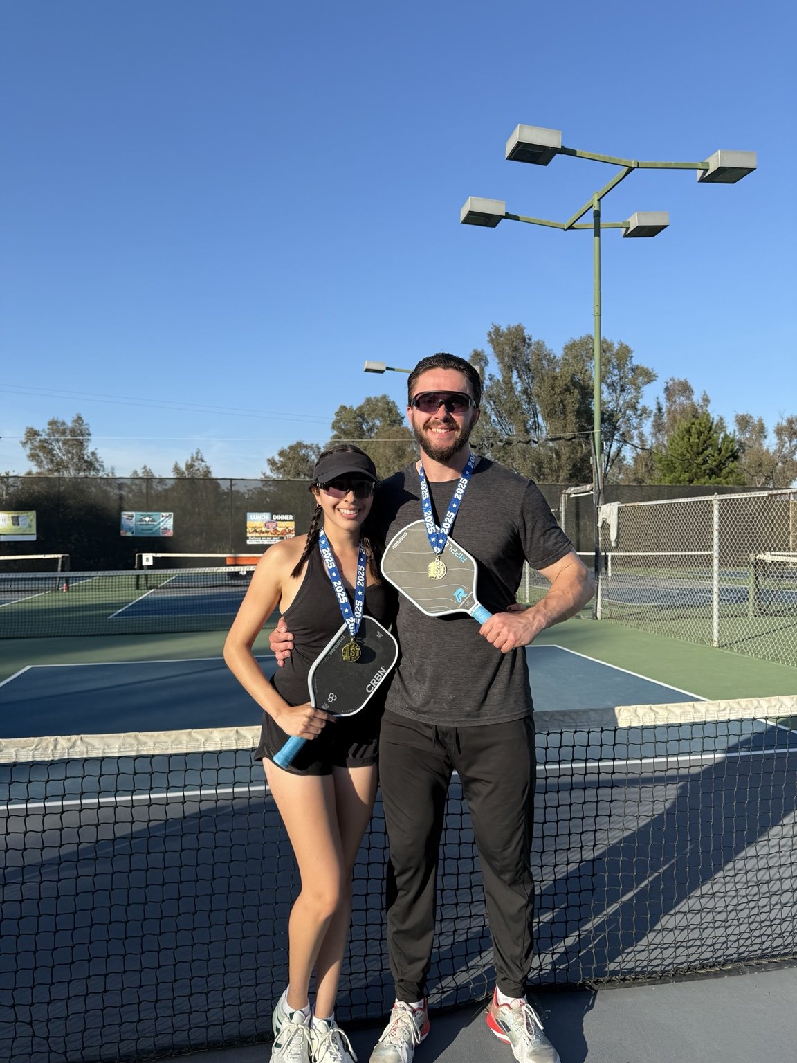 Arden Light and Elitza Lopez holding paddles and wearing medals on a pickleball court.