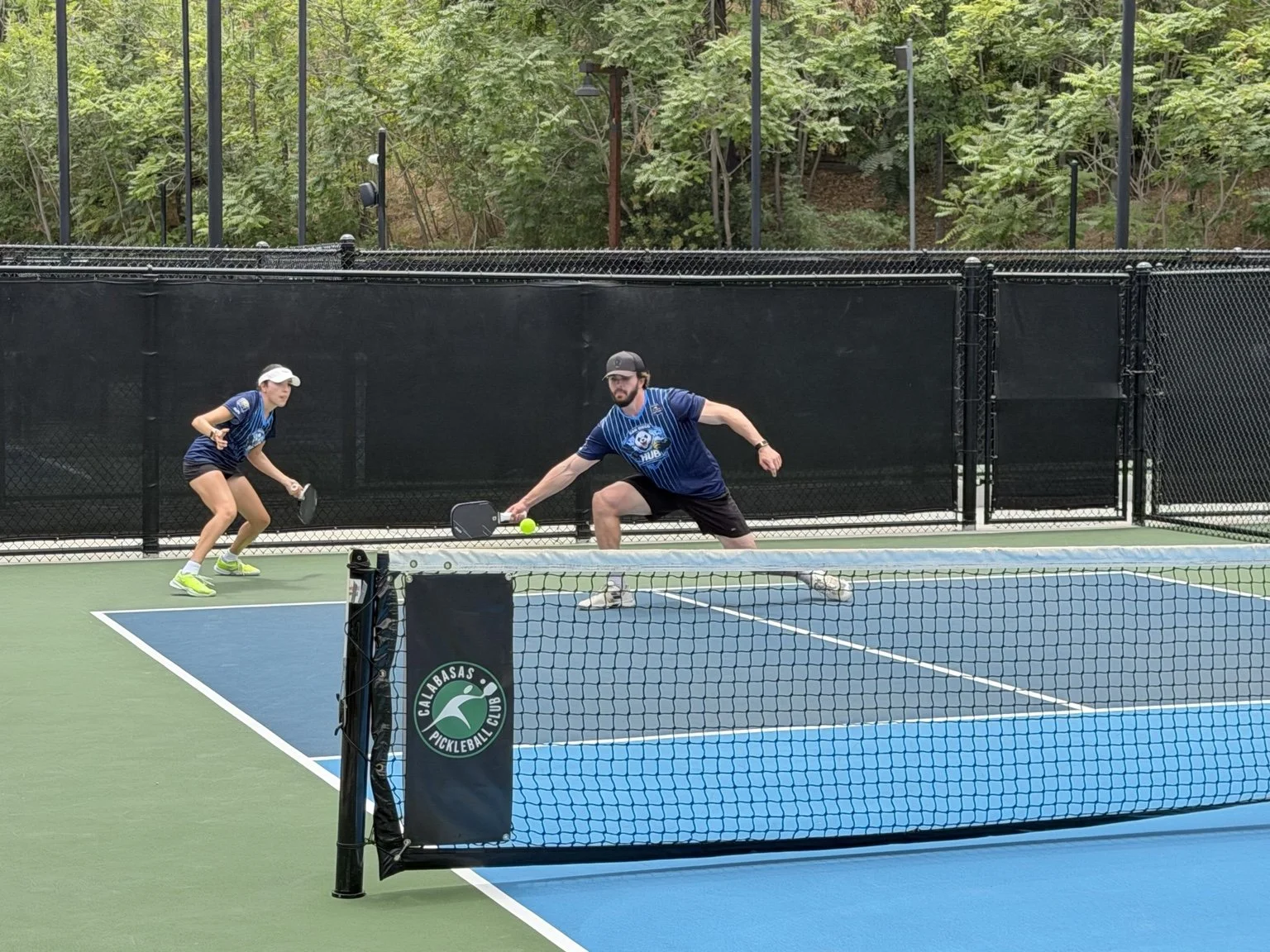 Arden Light reaching for a low ball during a doubles pickleball rally.