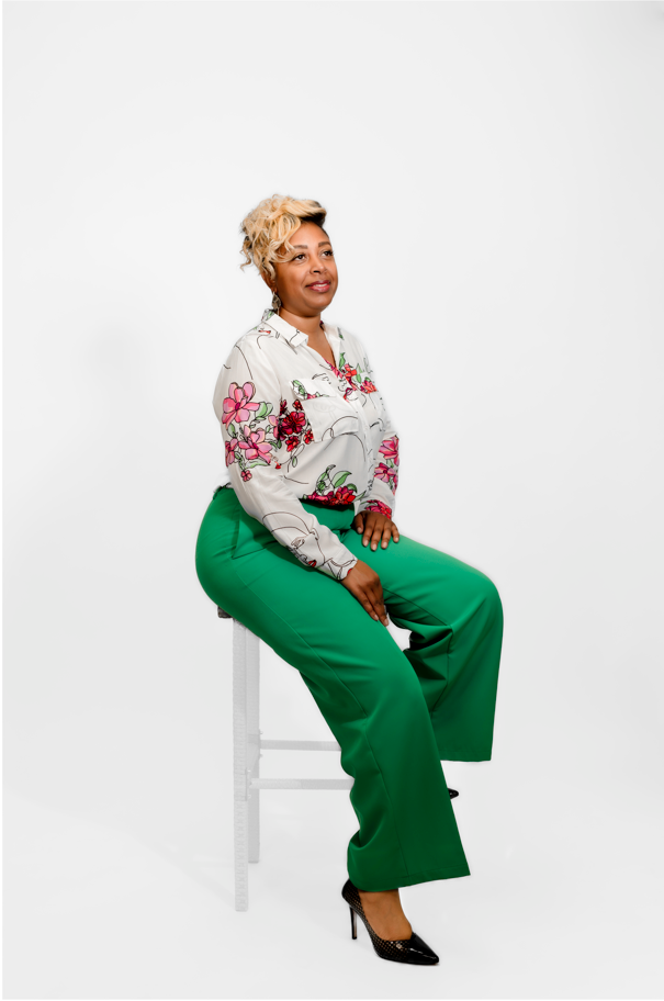 Woman sitting on a stool wearing a floral blouse and green pants