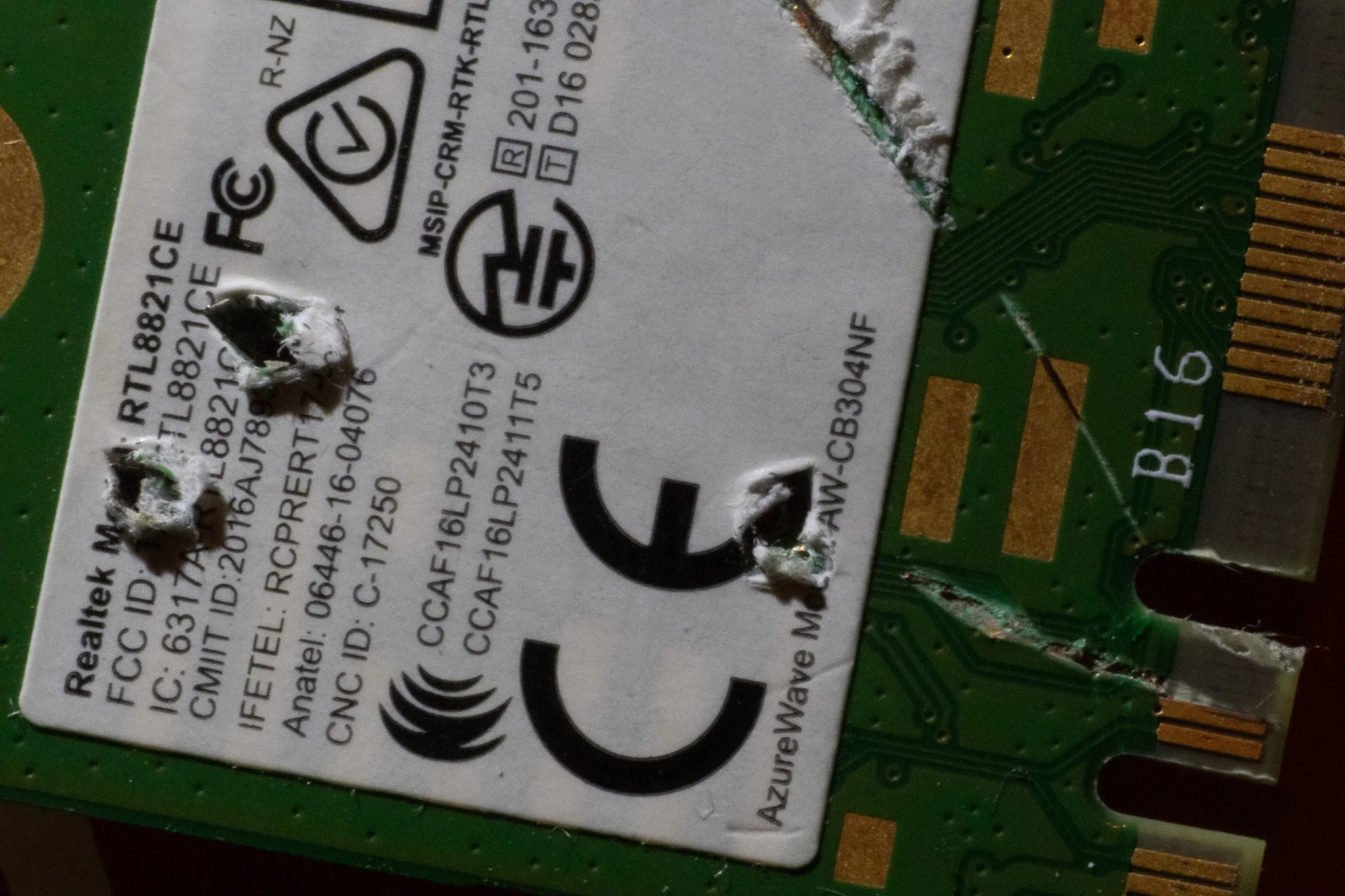 Close-up image of a damaged computer wireless network card with torn label and visible green circuit board with gold connectors.