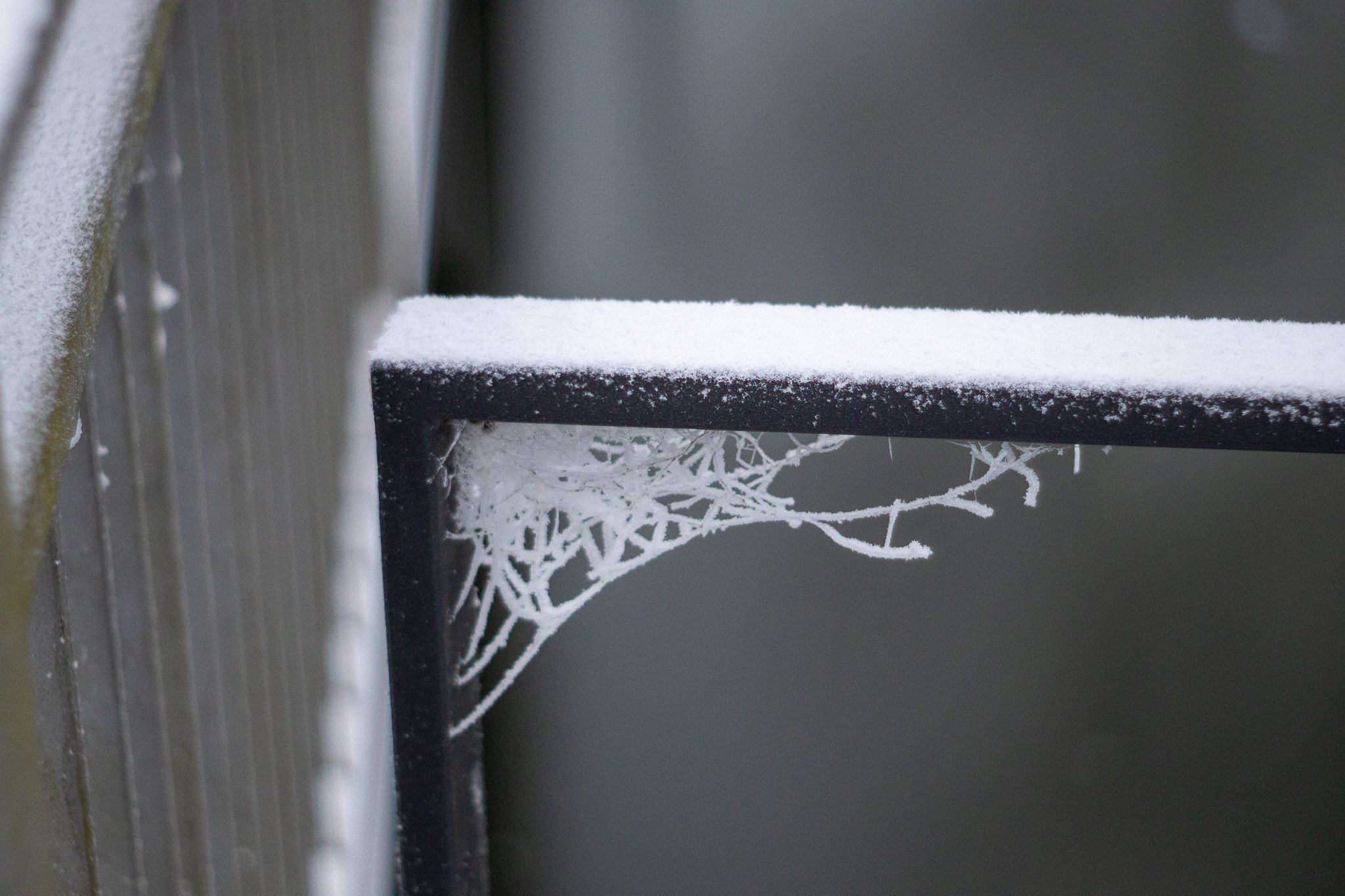 Close-up of a snow-covered balcony railing with frost patterns on the metal support.