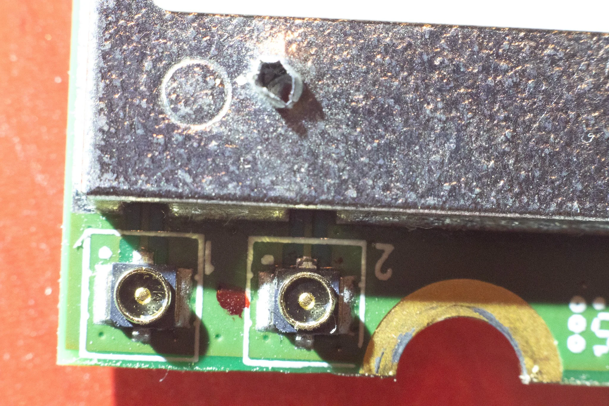 Close-up of a circuit board with two gold-plated connectors and a black component mounted on it, with a red background.