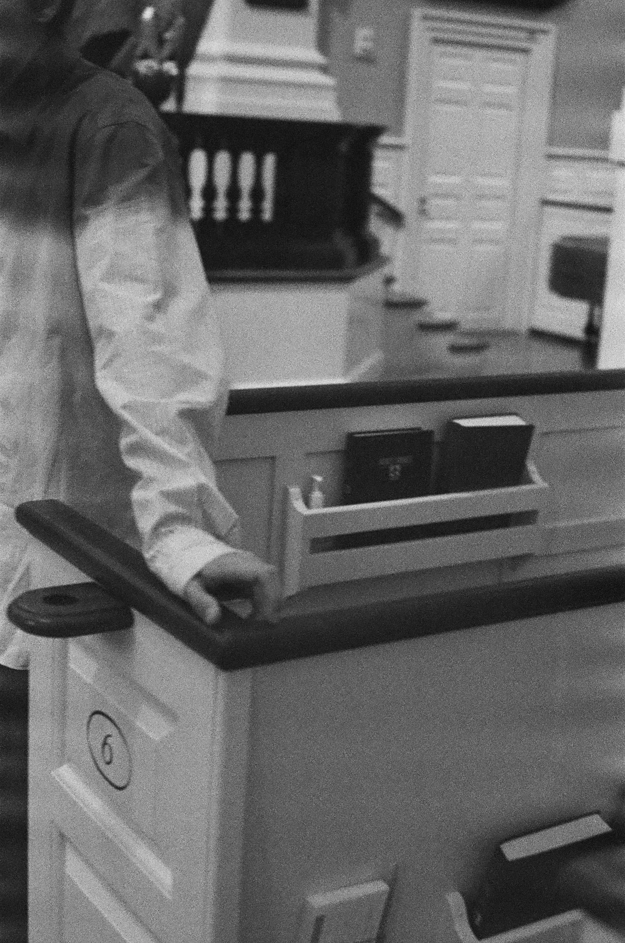 A person wearing a jacket operating a hospital or medical cart in a room with kitchen cabinets and appliances.
