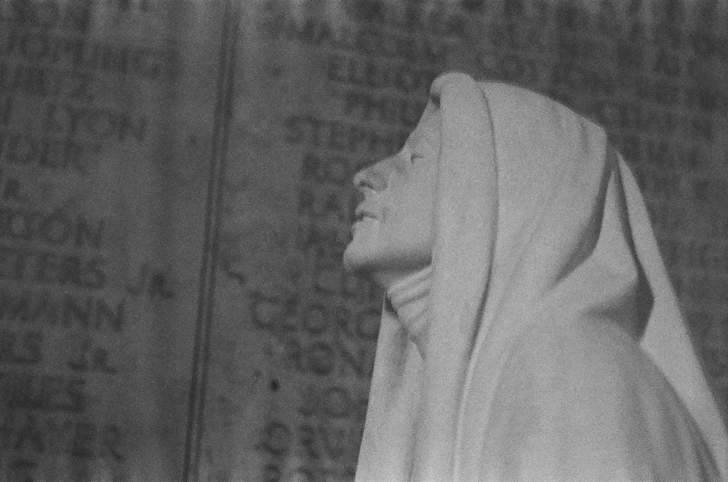 A woman in a hijab smiling in front of a brick wall with graffiti.