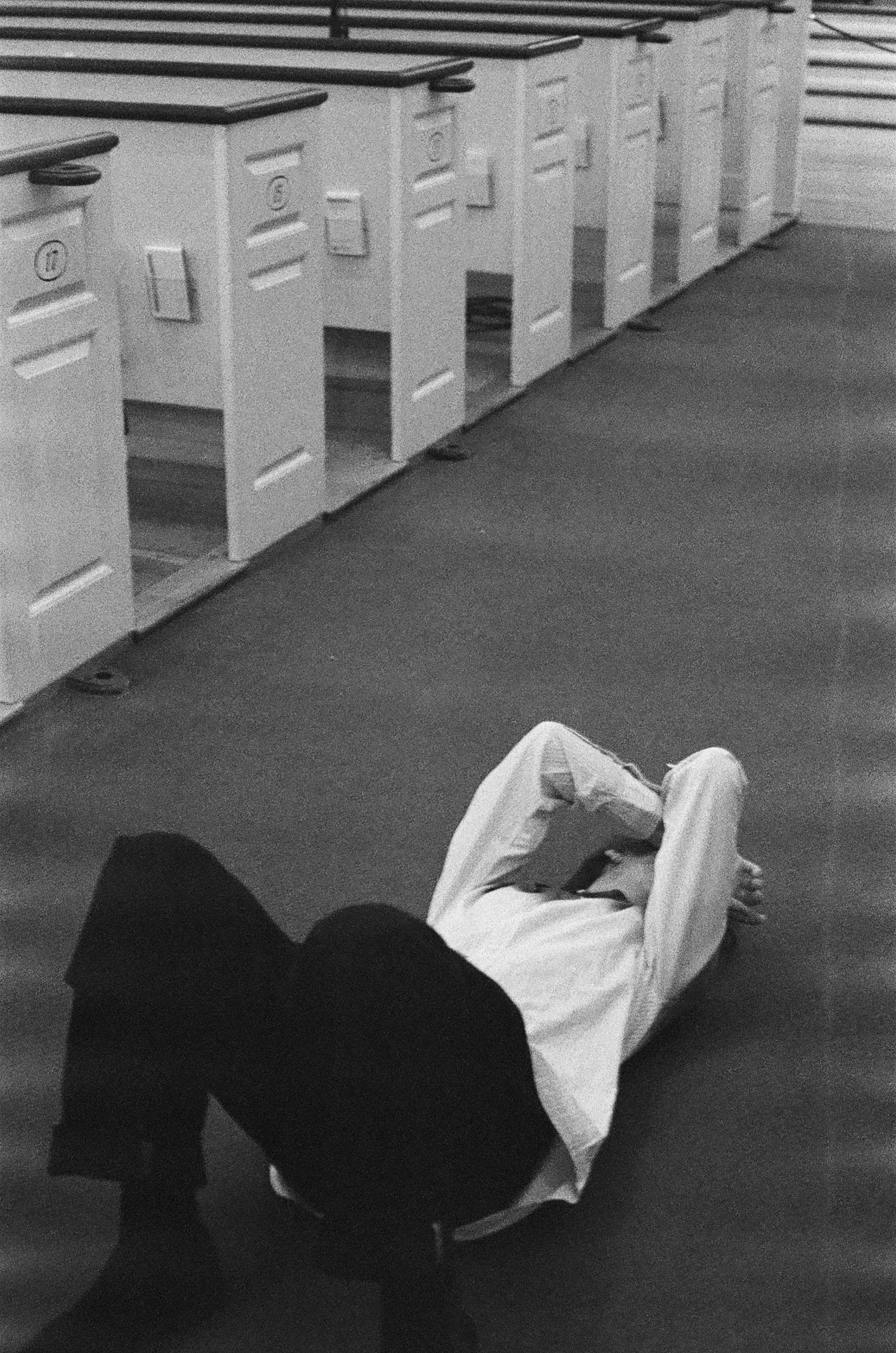A person lying on the floor with arms crossed over their face in a hallway with lockers.