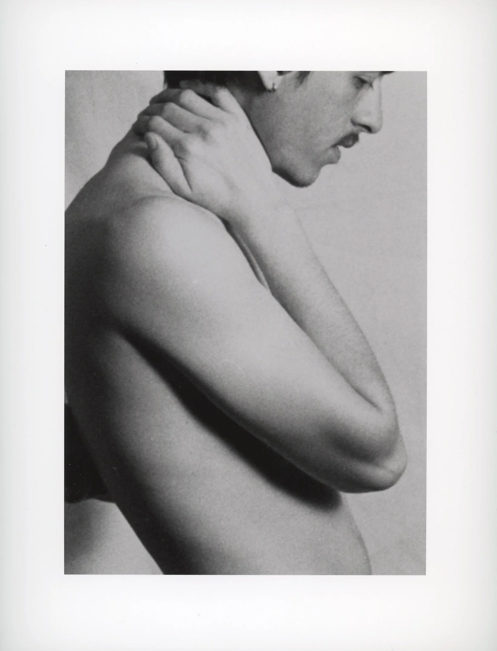 Black and white photo of a person with short hair, holding their neck with one hand, facing the right side.