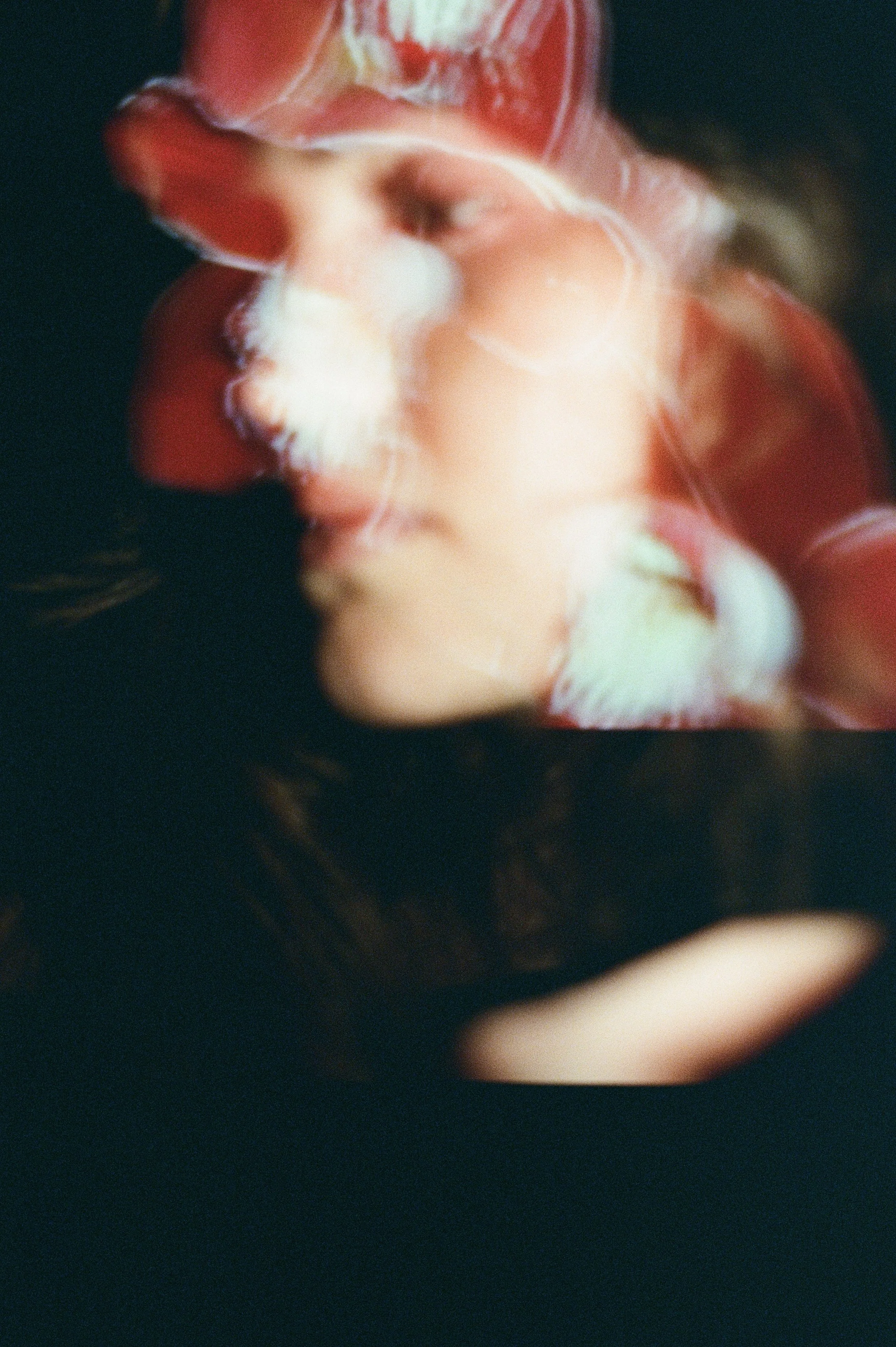 An abstract, blurry image of a person with their eyes closed, surrounded by swirling red, white, and beige colors.