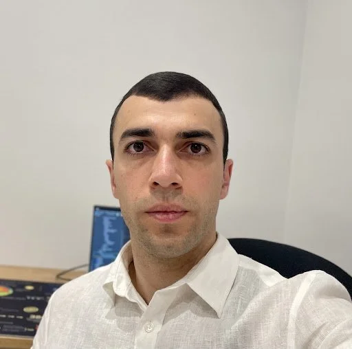 Man in a white shirt sitting at a desk in an office setting, looking at the camera.