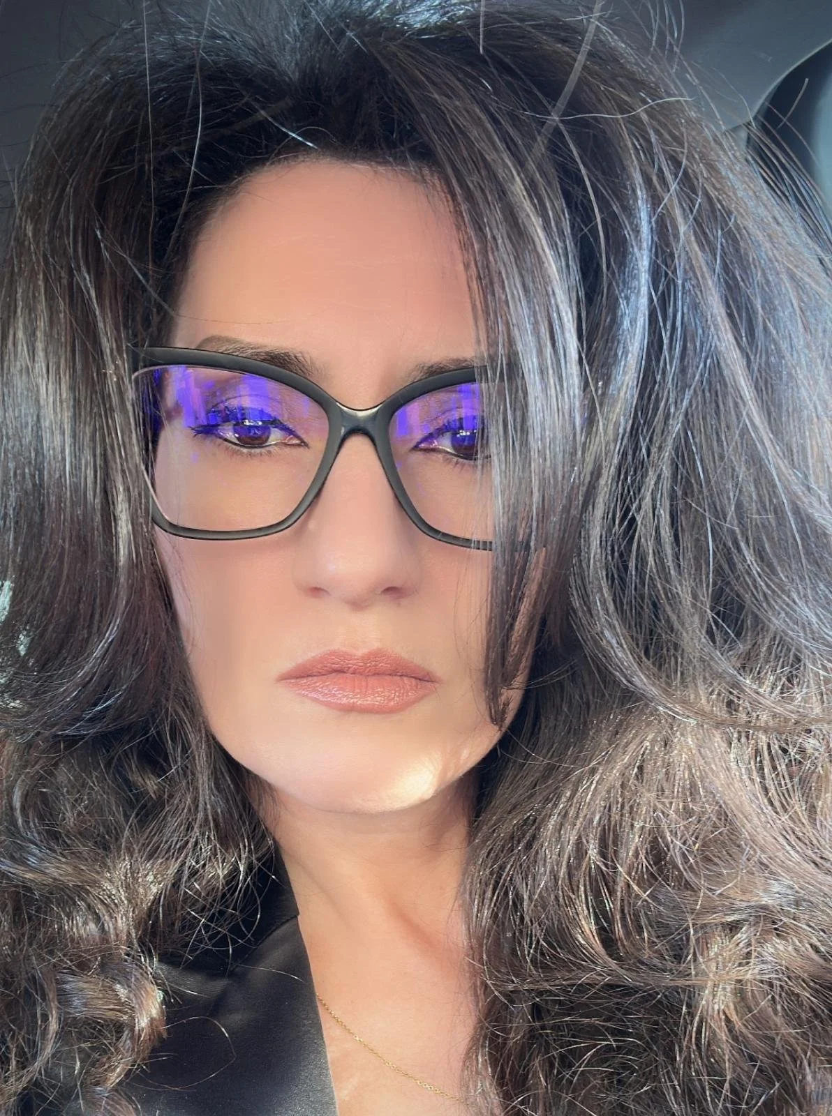 Close-up of a person with long, wavy hair wearing glasses and neutral makeup.