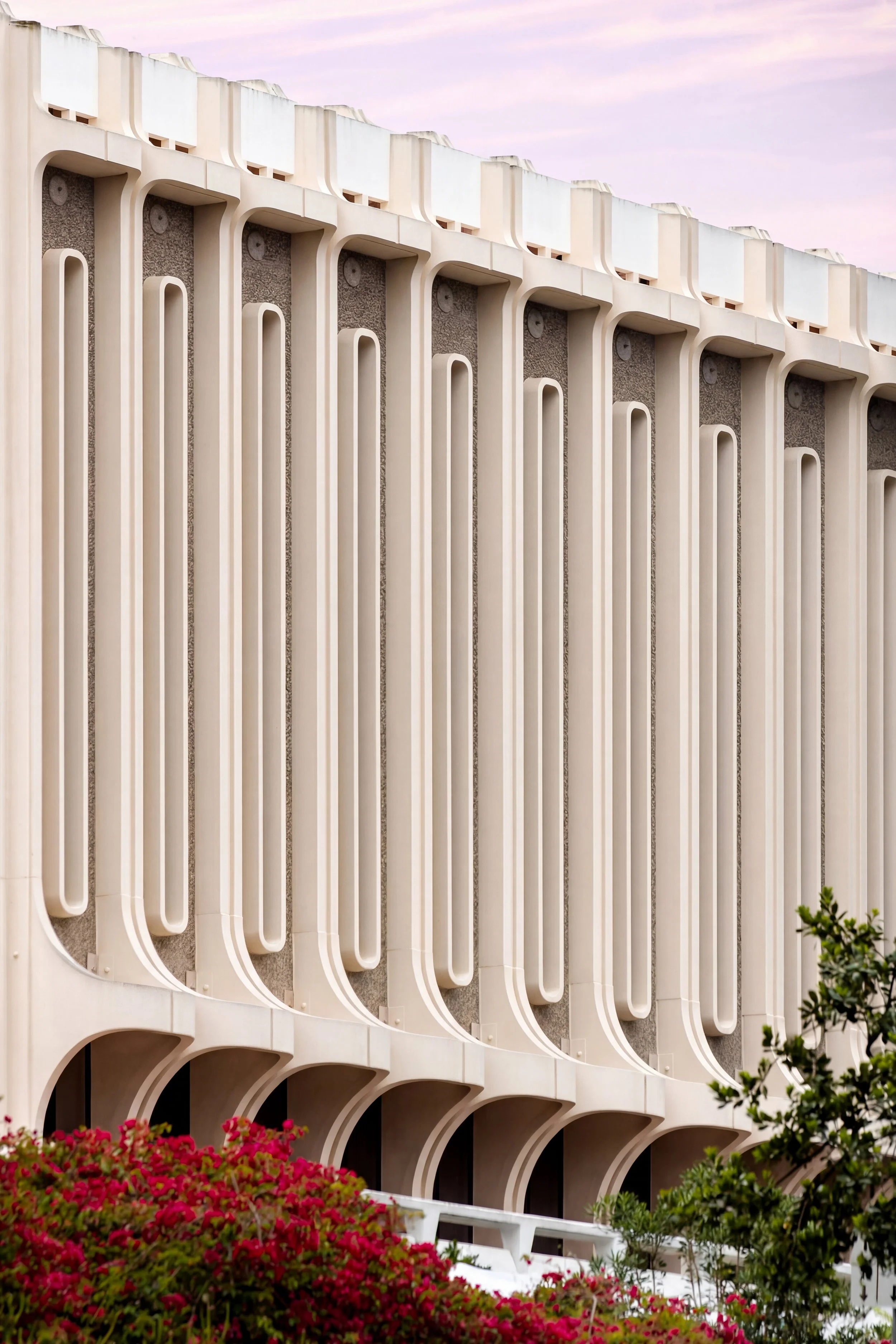 Exterior detail of Langson Library at UC Irvine, featuring brutalist, mid-century modern architecture with vertical concrete fins and soft pastel sky.