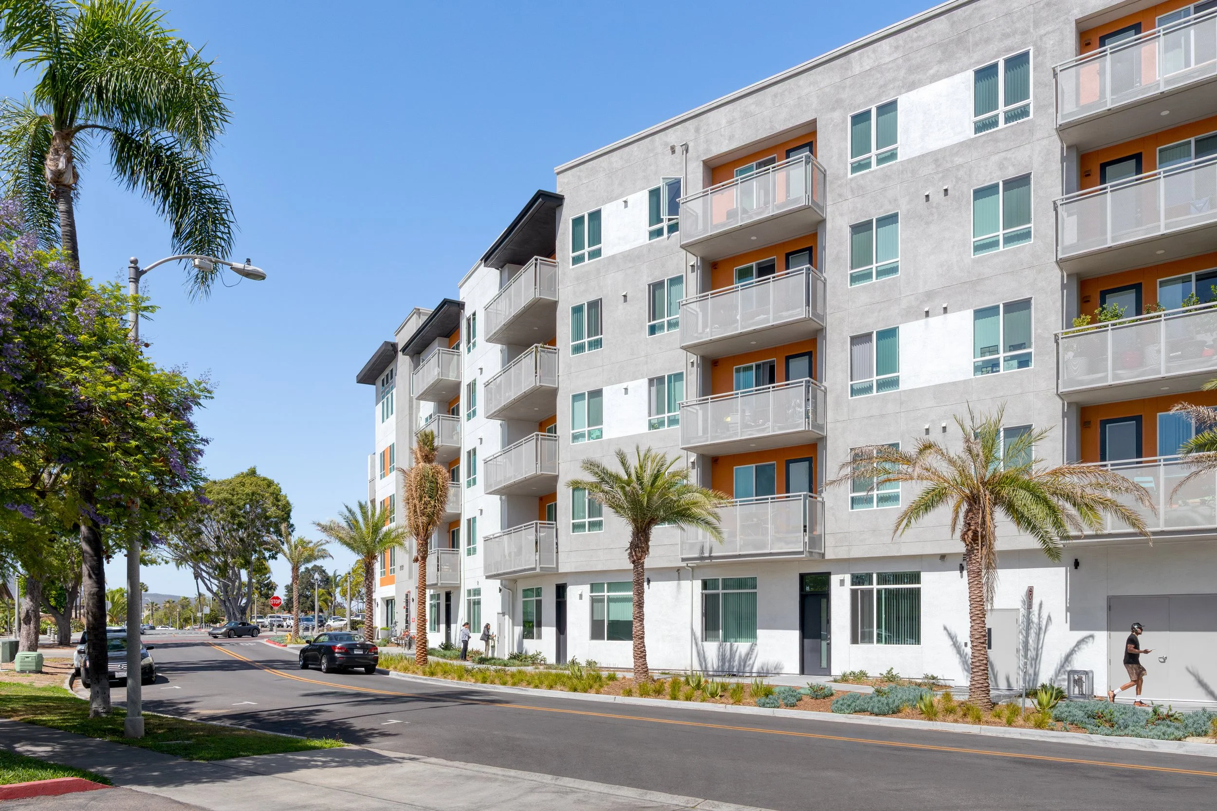 Contemporary multi-story residential apartment complex in La Mesa, CA featuring metal balconies with orange accents along a palm-lined street.