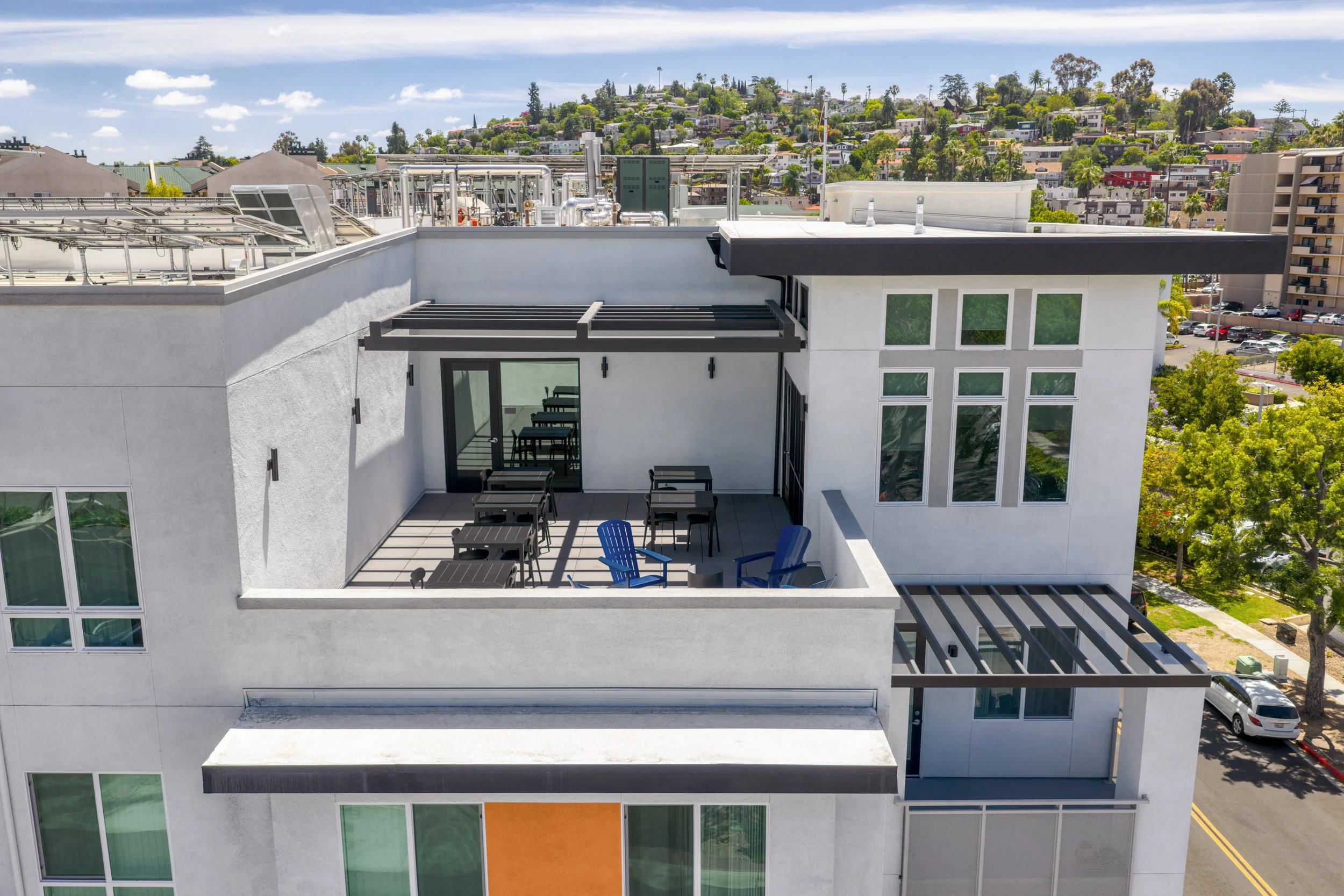 Aerial view of an apartment rooftop deck amenity space in La Mesa, CA showing seating areas and solar panels on the adjacent roof.