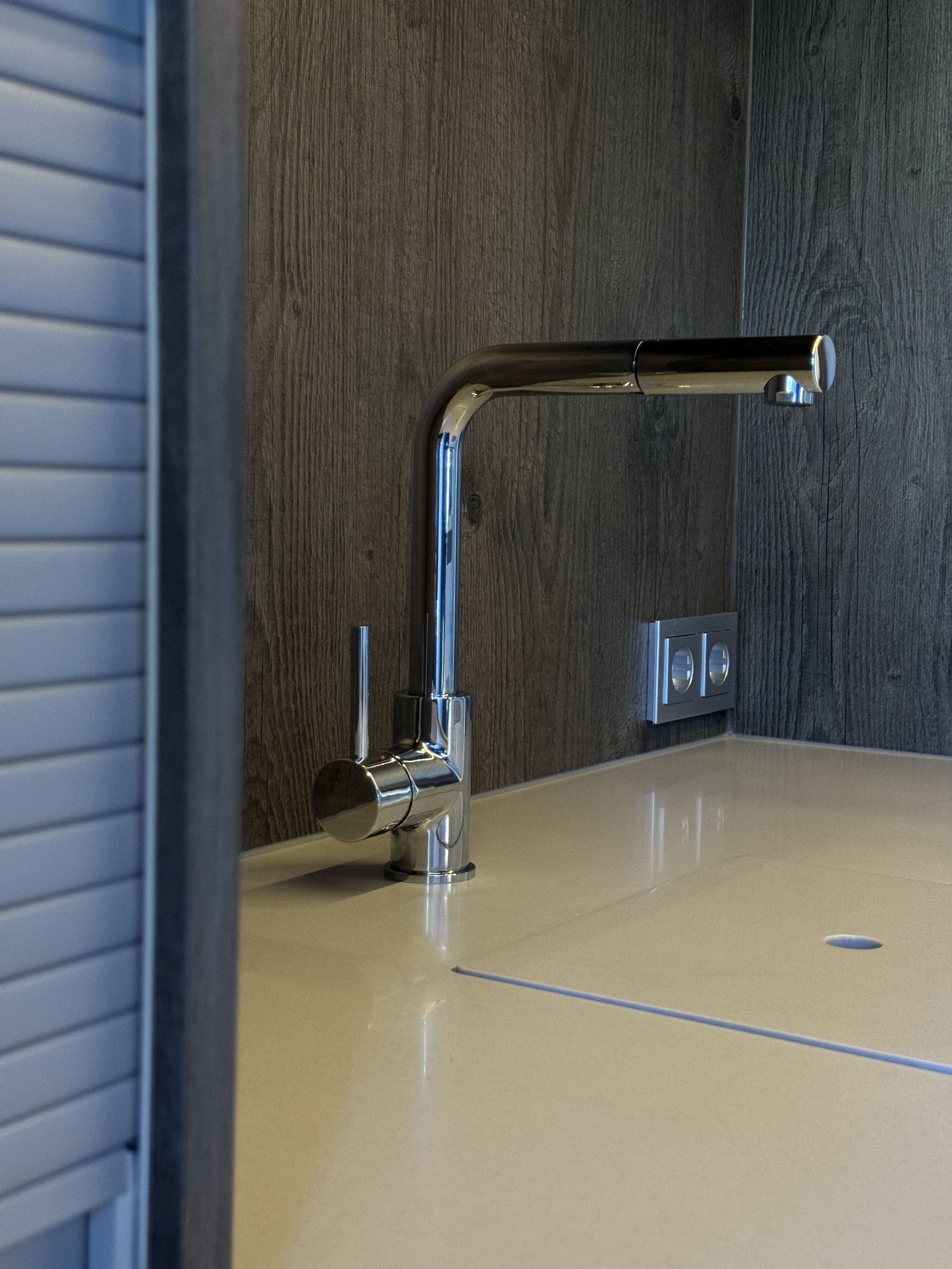 Moderne Küche mit Edelstahlarmatur auf einer weißen Arbeitsplatte und einer Holzrückwand.