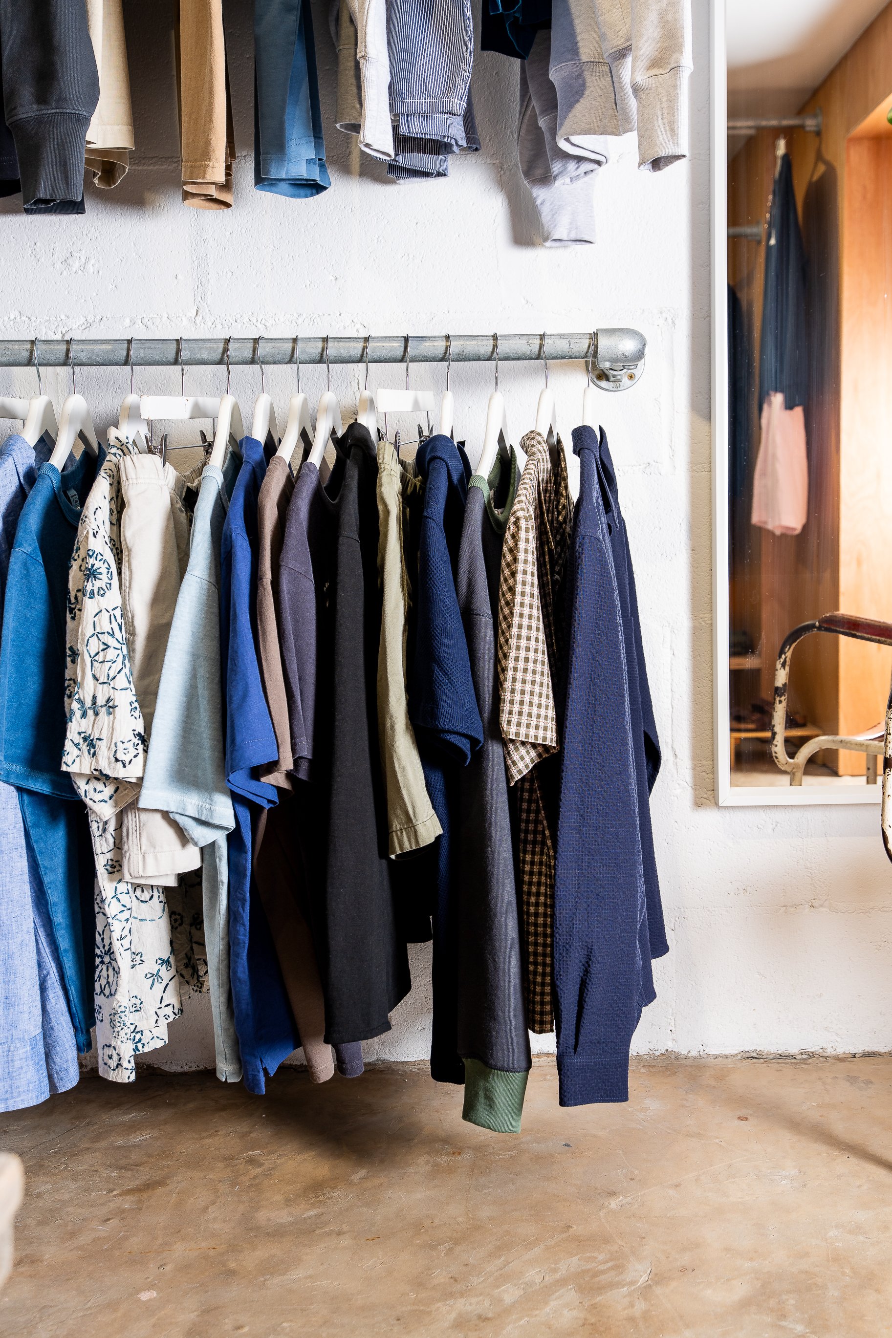 Clothes hanging on a rack inside a store or closet, with a mirror reflecting some additional clothing items.