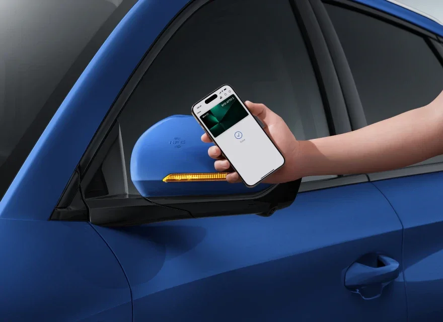 Person holding a smartphone near the side mirror of a blue car, with a wireless sensor device attached to the mirror.