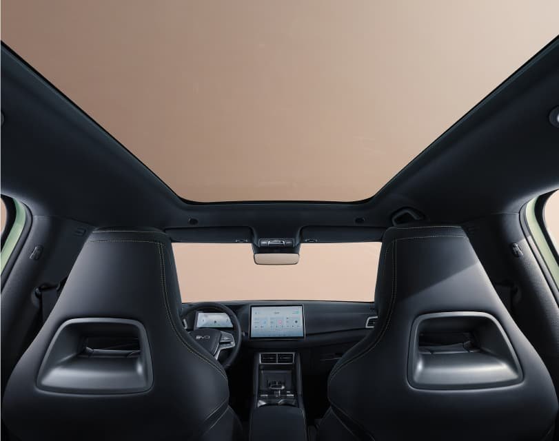 Wnętrze modelu BYD Atto 2 z perspektywy tylnej kanapy, ukazujące duży, przeszklony dach panoramiczny, zintegrowane sportowe fotele oraz deskę rozdzielczą z centralnym ekranem na jasnym tle.